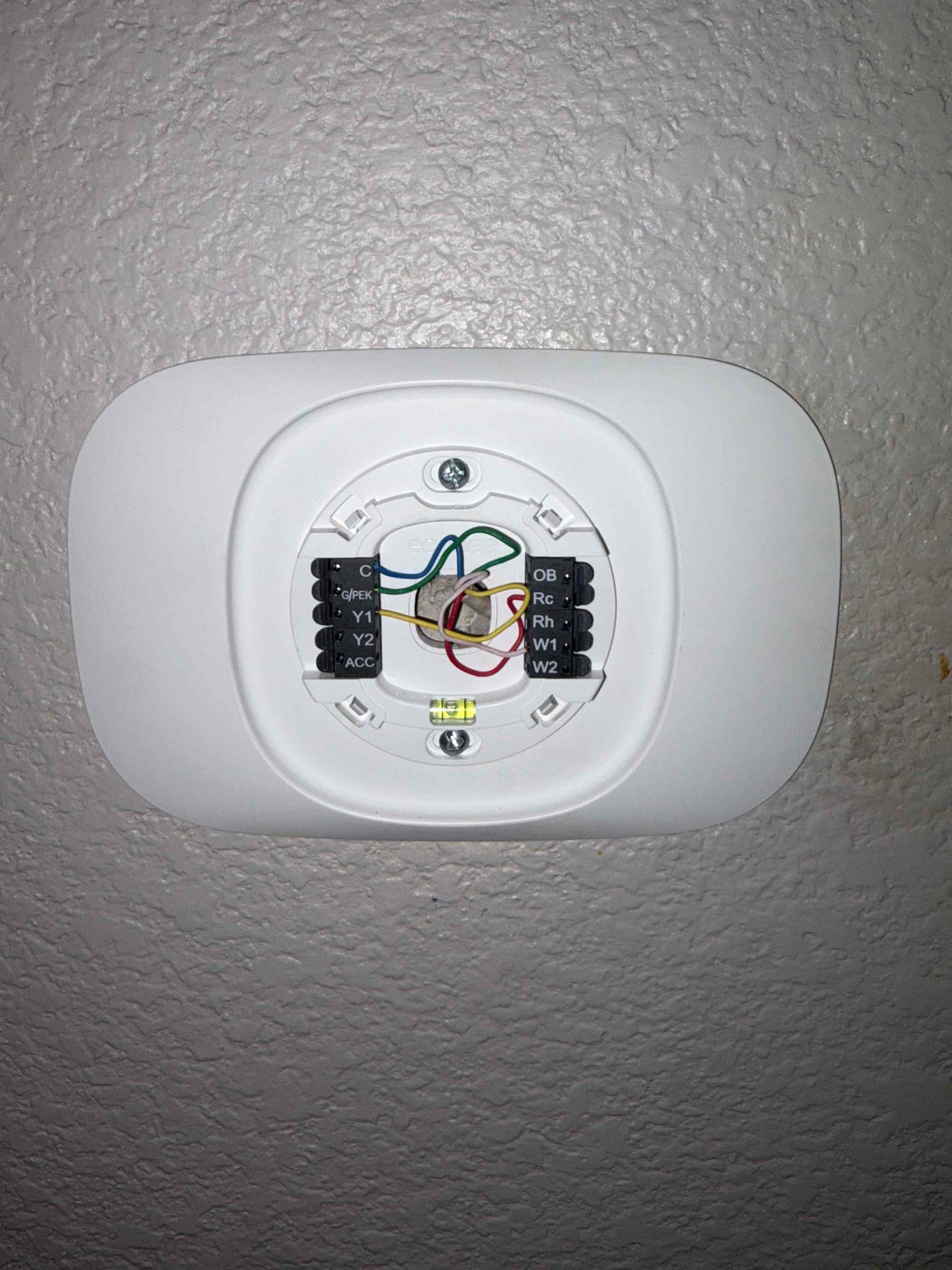 Thermostat wall plate installed with colored control wires connected to labeled terminals and built-in bubble level visible.