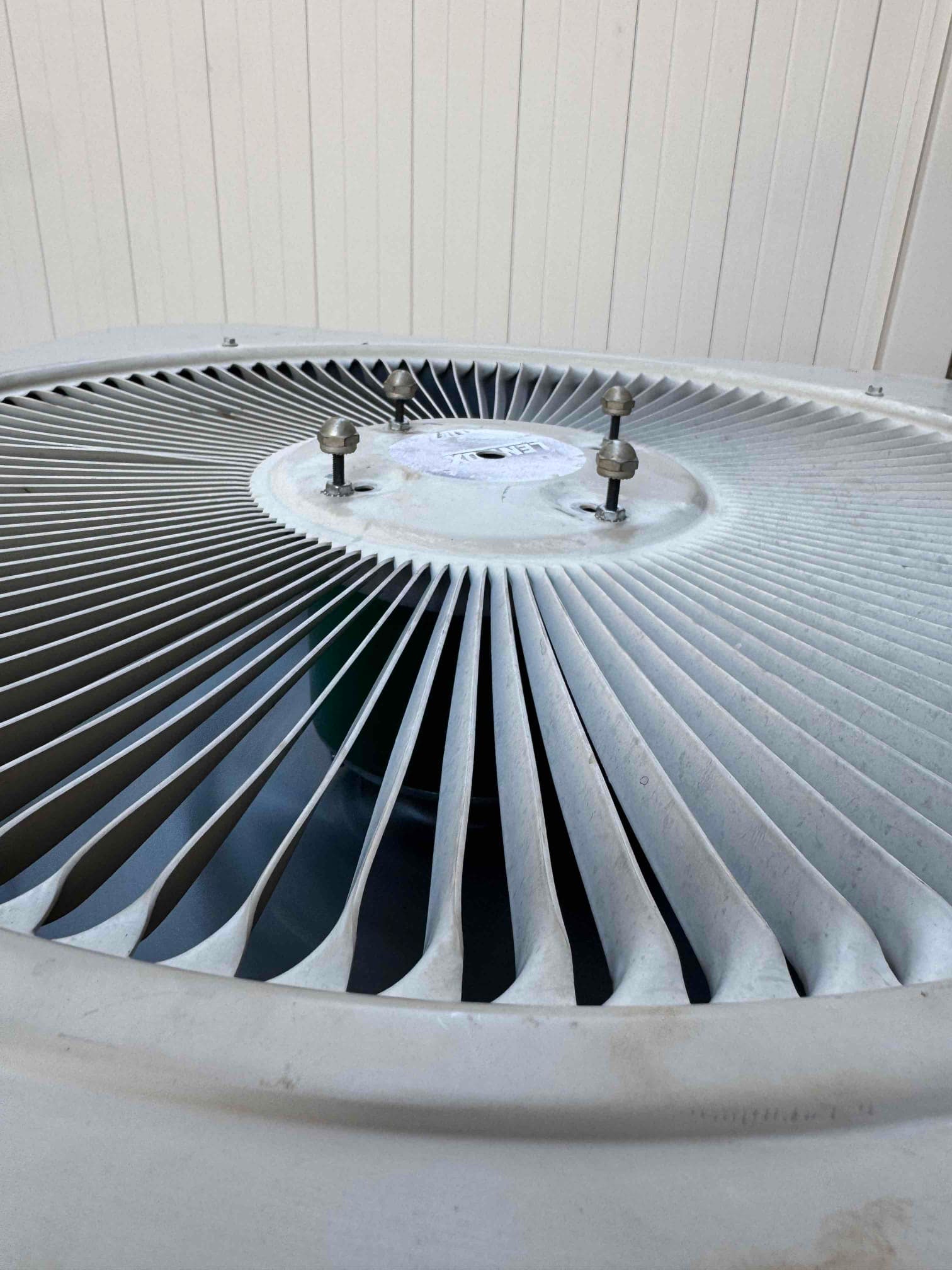 Top view of outdoor condenser fan guard and hub, with mounting bolts and accumulated surface dust.