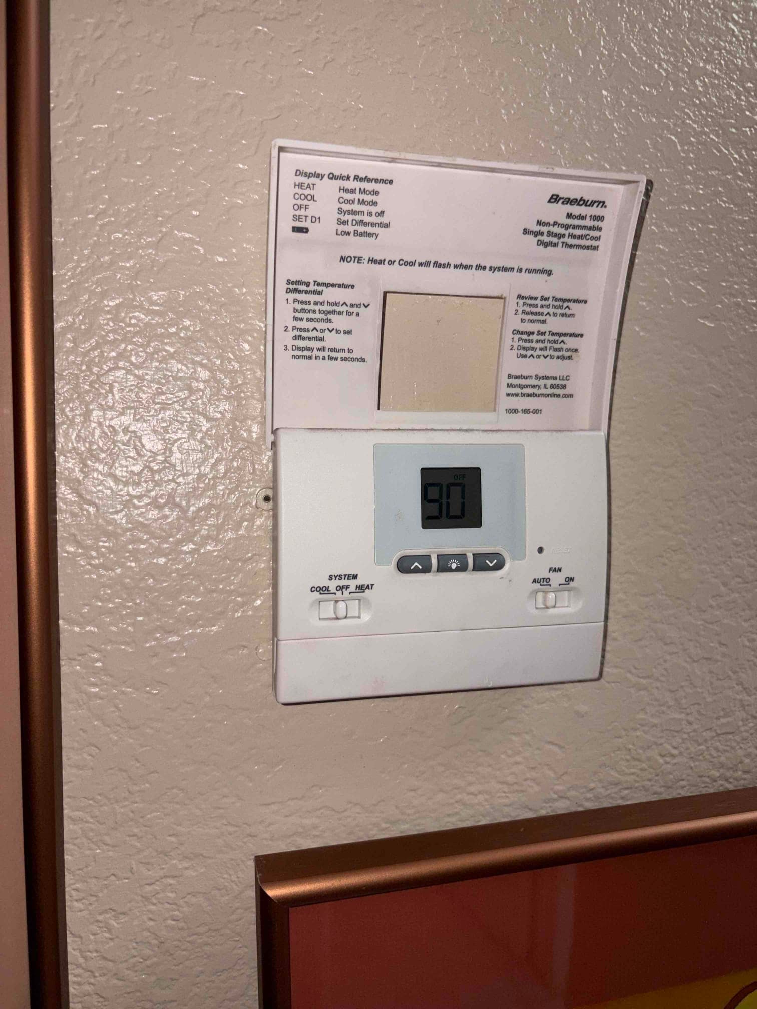 Wall-mounted digital thermostat with cover open, display shows 90 and mode and fan switches visible.