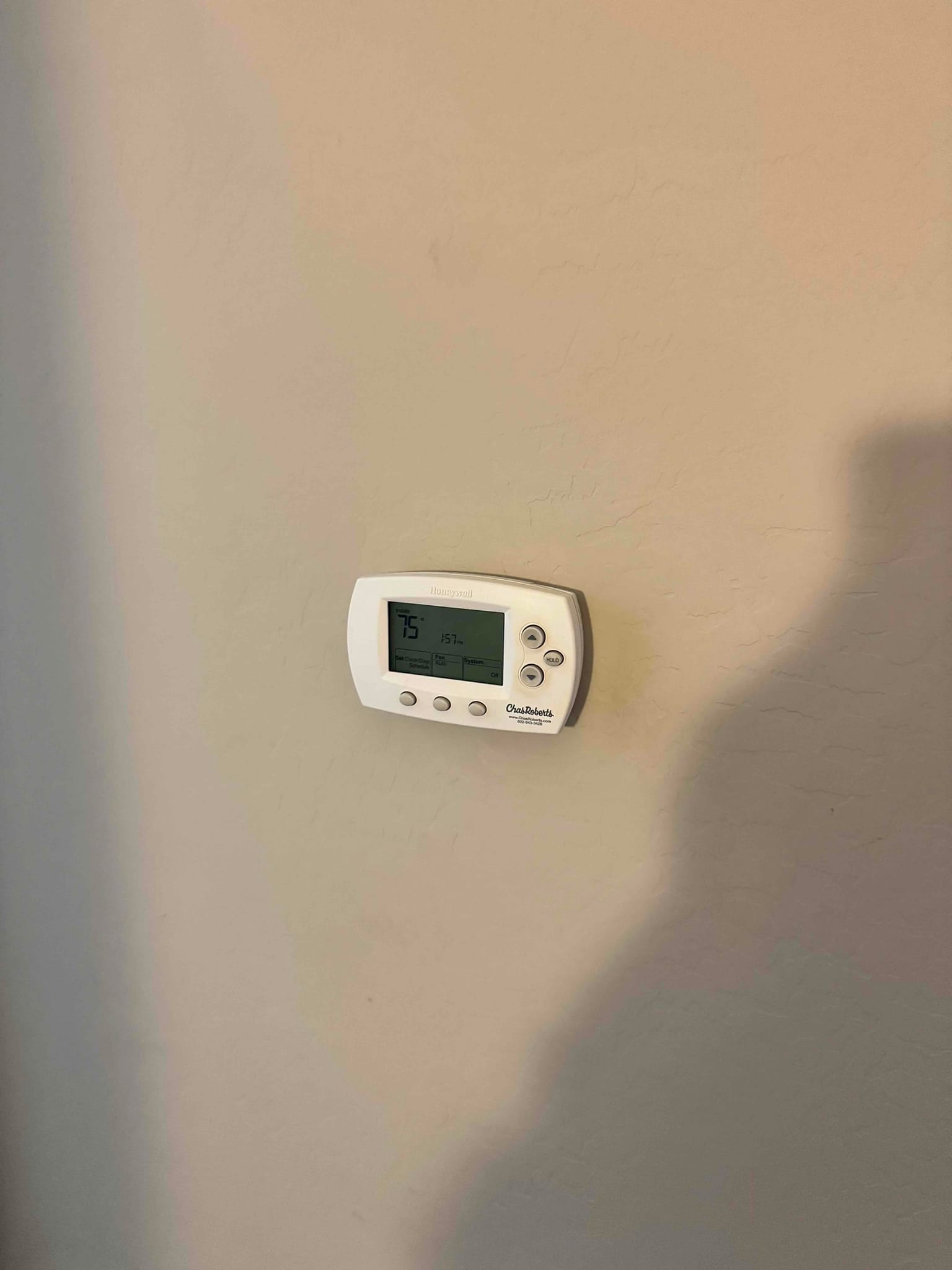 Wall-mounted digital thermostat with display showing 75°F and mode icons, installed on a painted interior wall.