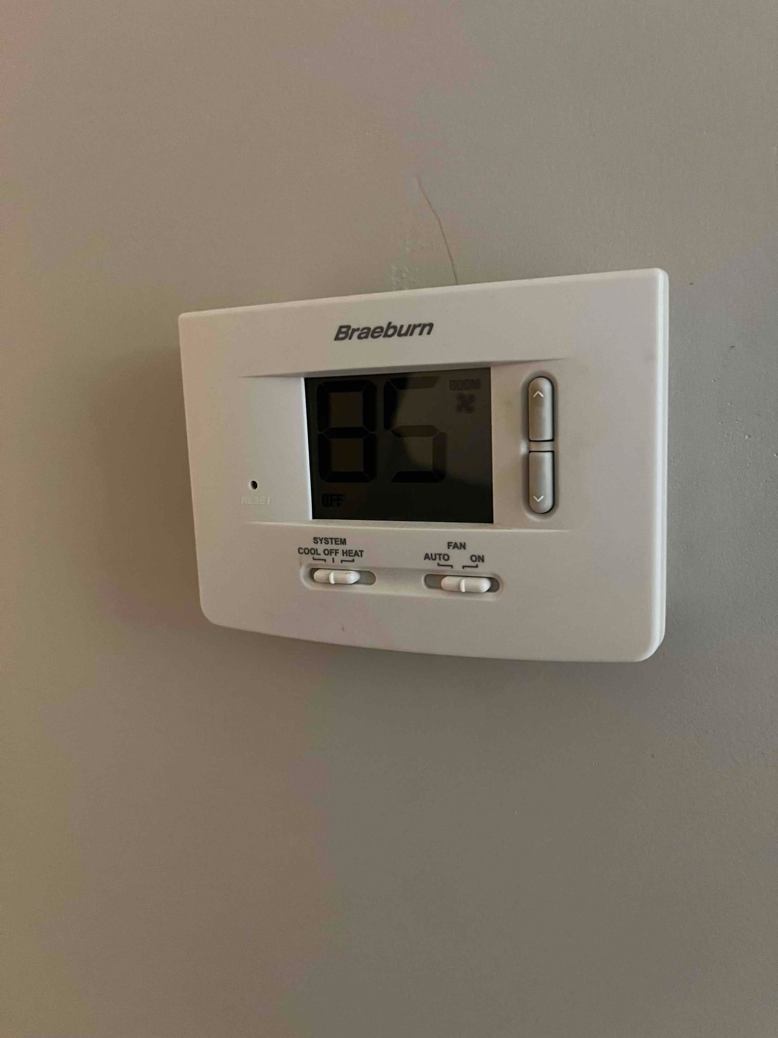 Wall-mounted digital thermostat displays 85 with system switch set to OFF and fan set to AUTO.