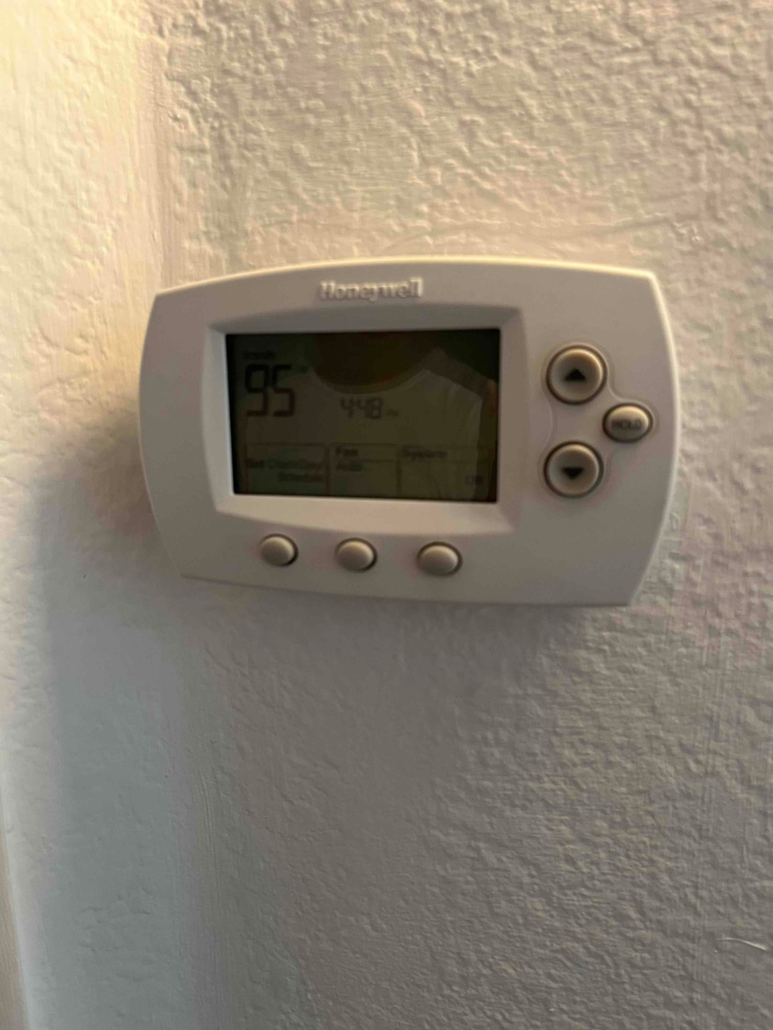 Wall-mounted digital thermostat shows 95°F on the display with control buttons and system, fan, and hold indicators.