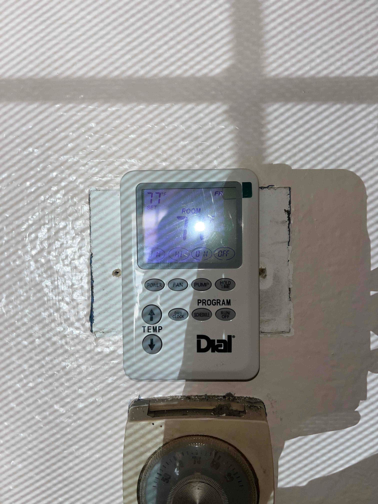 Wall-mounted digital thermostat shows set 77°F and room 77°F with control buttons; an older analog dial thermostat remains installed directly below.
