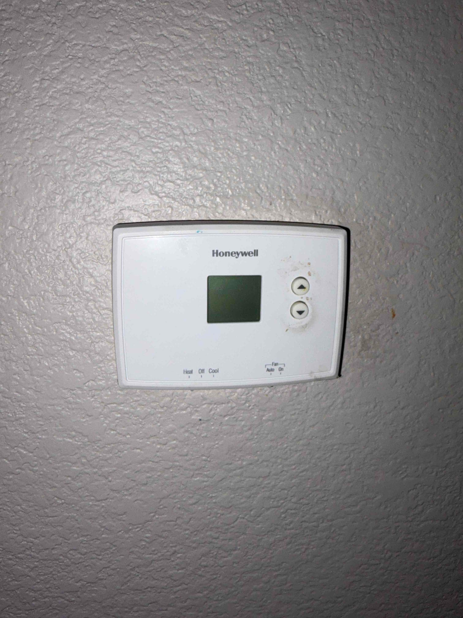 Wall-mounted digital thermostat with small display and two buttons, showing Heat/Off/Cool and Fan Auto/On selectors.