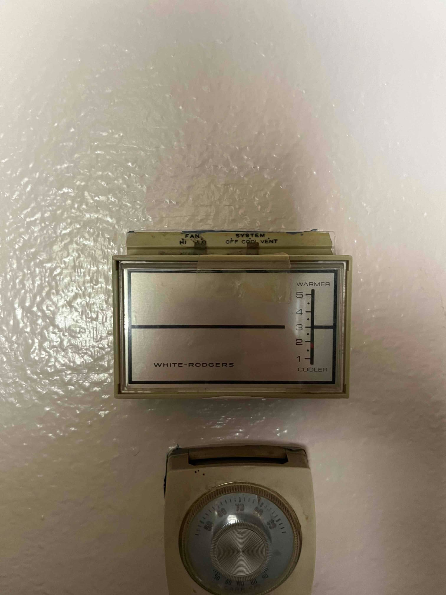 Wall-mounted mechanical thermostats with fan and system switches and a temperature dial below.