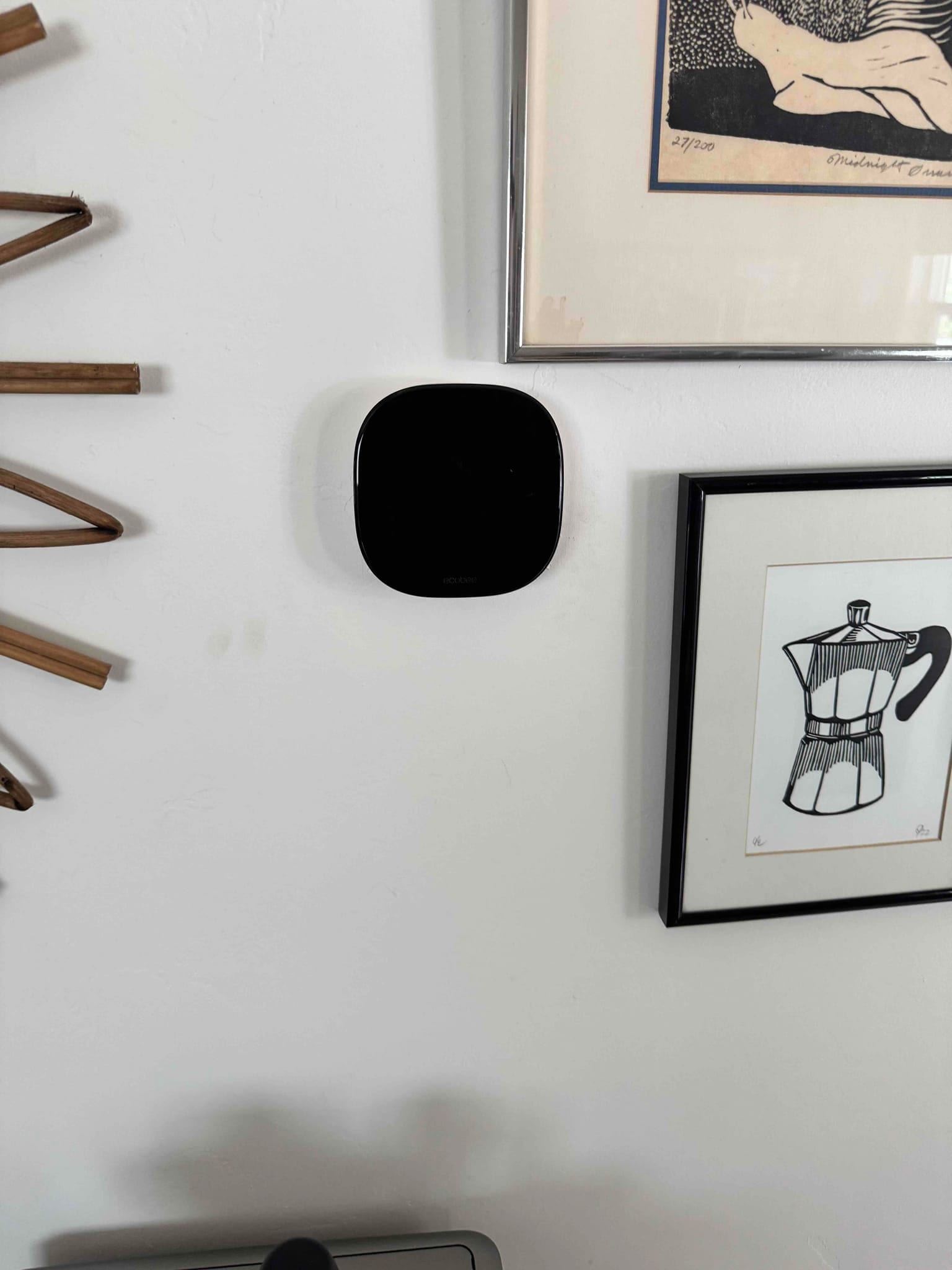 Wall-mounted smart thermostat with blank display between framed artwork in a residential interior.