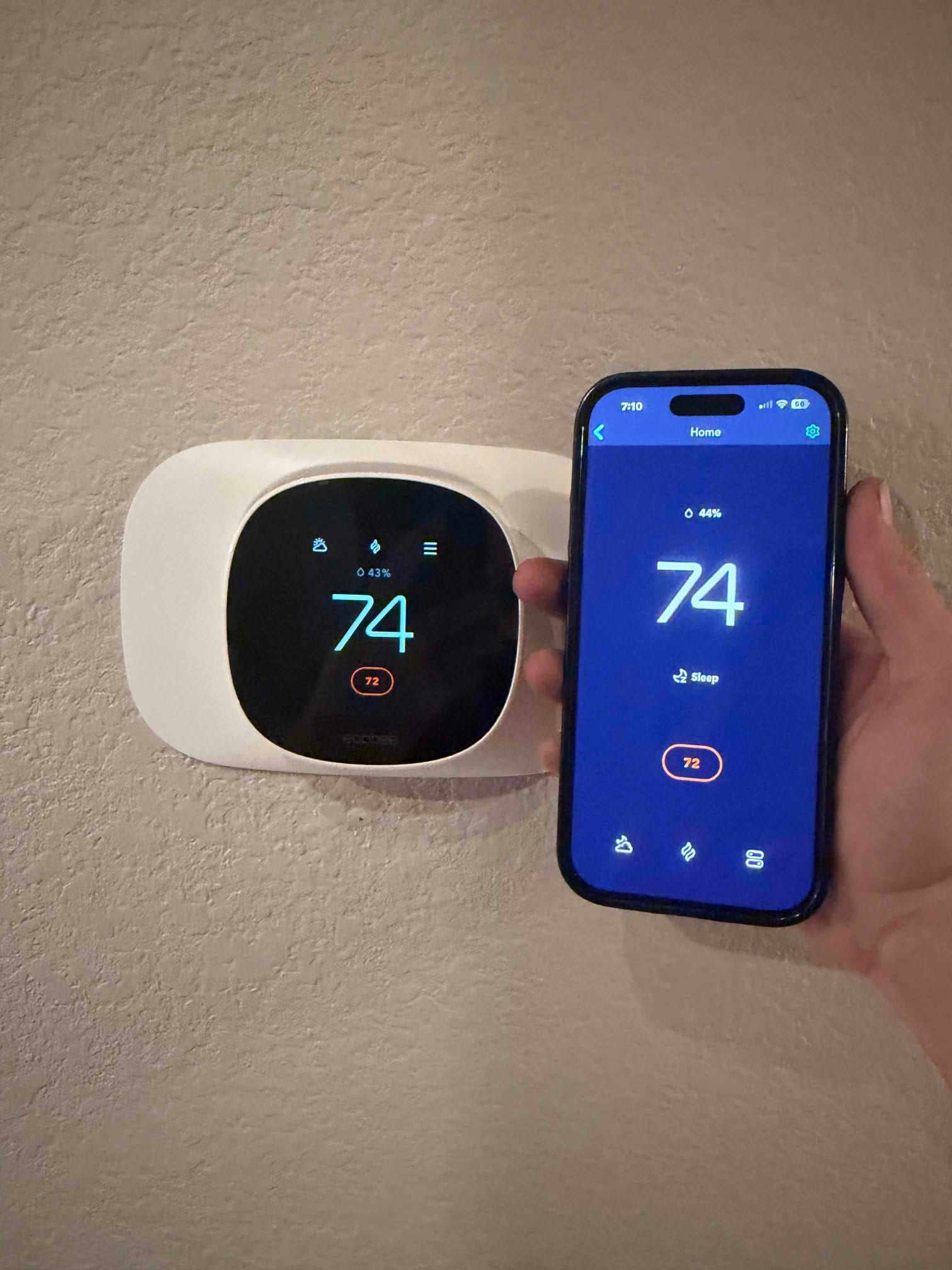 Wall-mounted smart thermostat displays 74 degrees, with a smartphone app beside it showing 74 and a 72 setpoint.