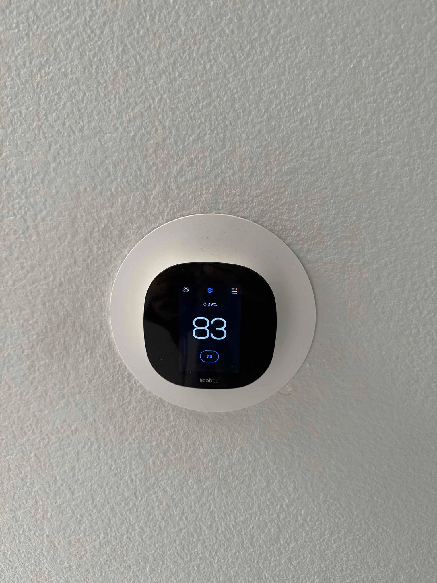 Wall-mounted smart thermostat displays 83° with cooling mode icon and a 75° set temperature.