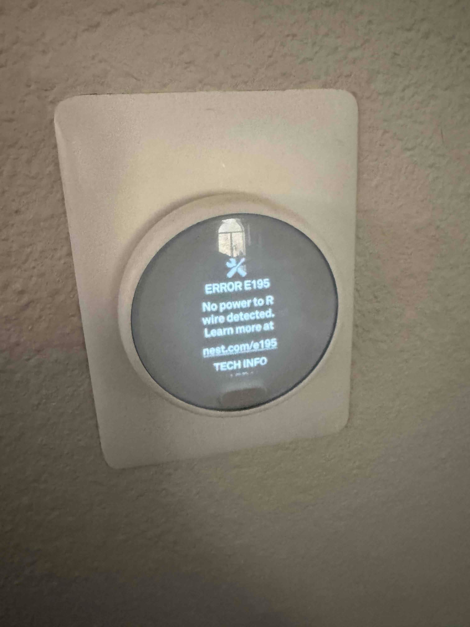 Wall-mounted smart thermostat displays error 'E195 No power to R wire detected' and prompts for technical information.