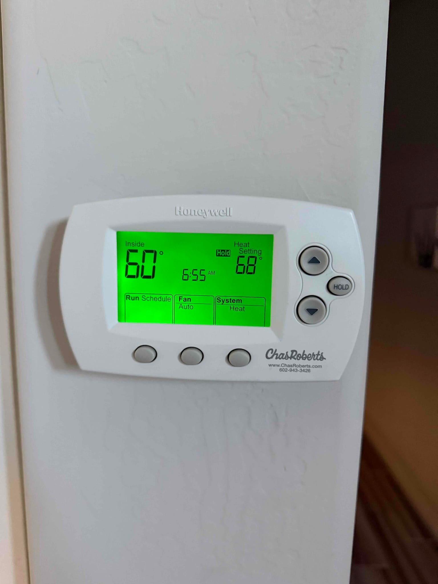 Wall-mounted thermostat displays inside 60°, heat setting 68°, Hold active with fan Auto and system Heat selected.