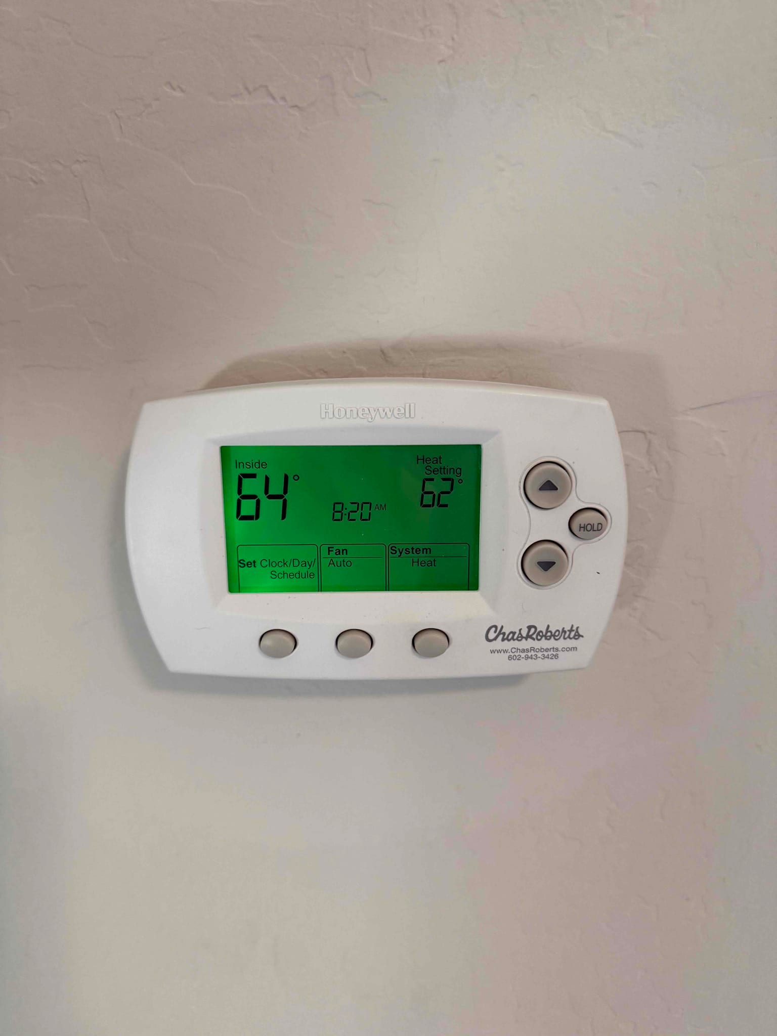Wall-mounted thermostat displays inside temperature 64°, heat setting 62°, fan set to Auto, system set to Heat.