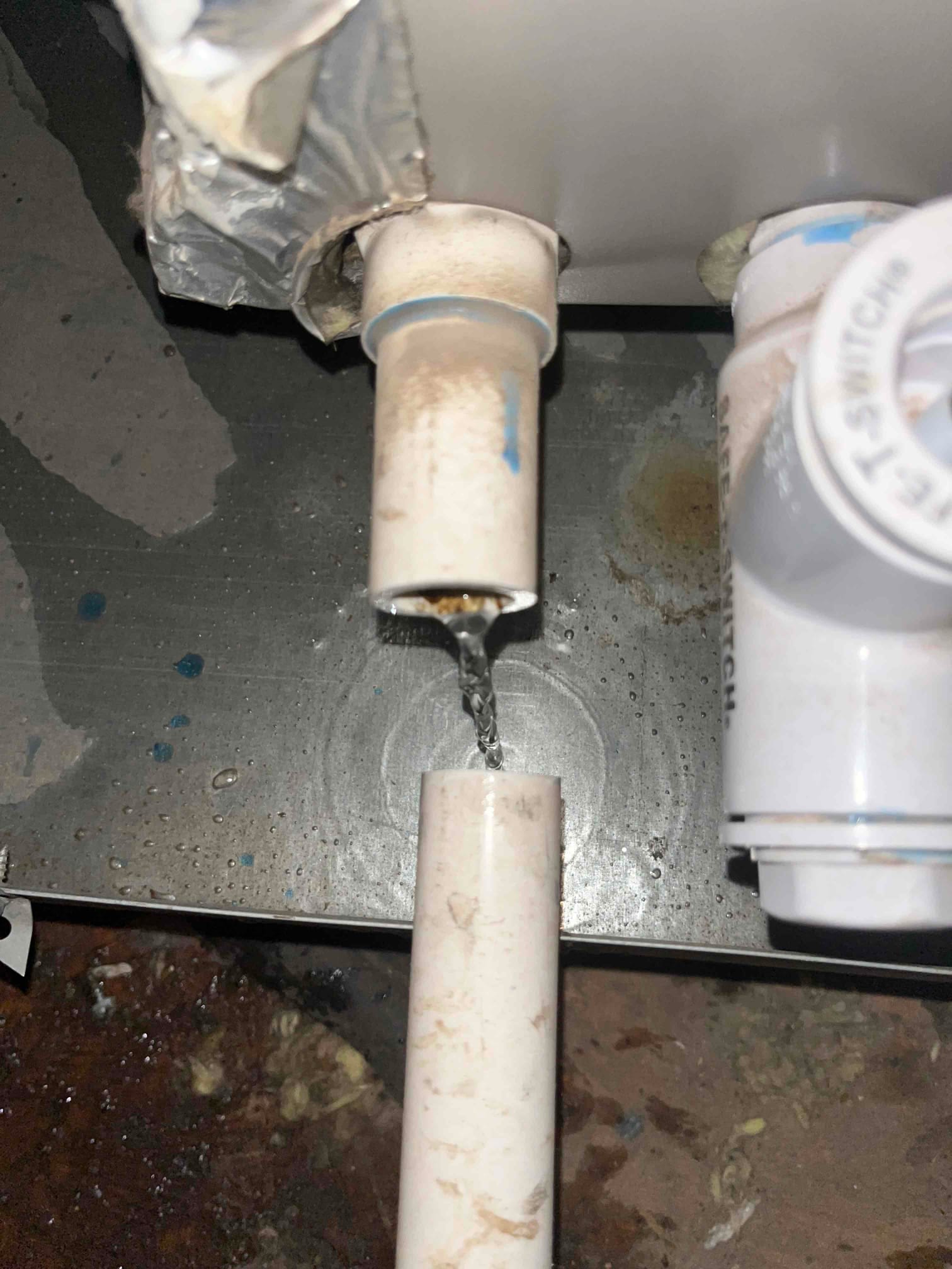 Water flows from an upper PVC condensate drain outlet into a lower PVC pipe beneath an HVAC unit.