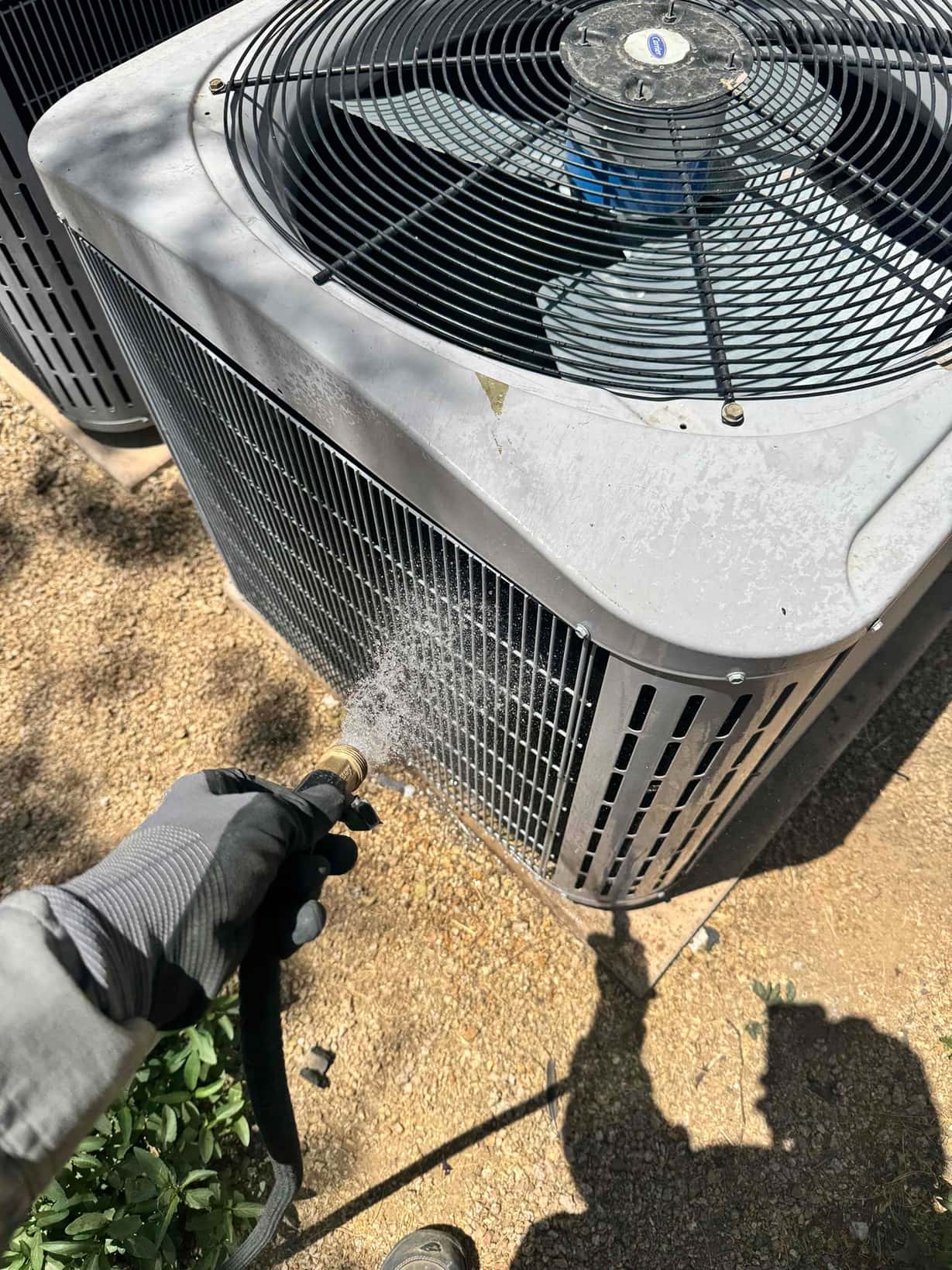 Water hose sprays the side condenser coil of an outdoor air conditioning unit.