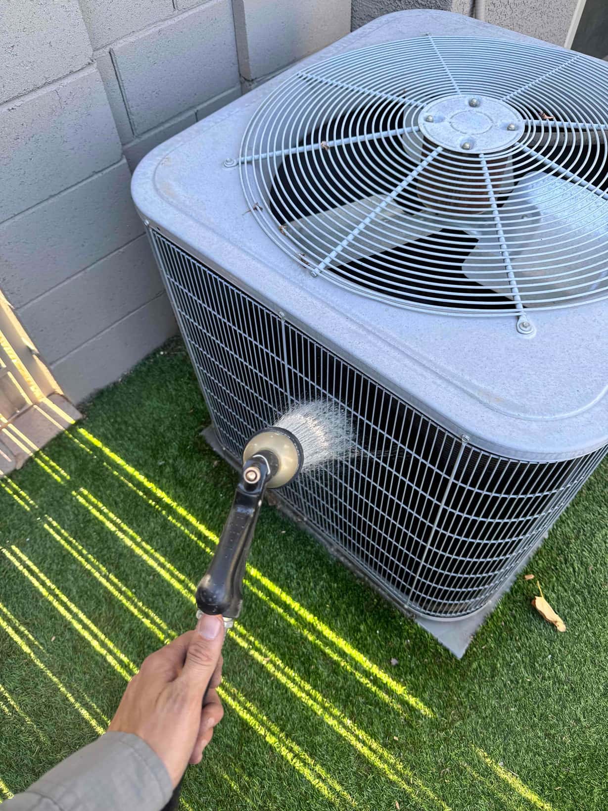 Water spray from a hose nozzle directed at the outdoor condenser coil and grille.