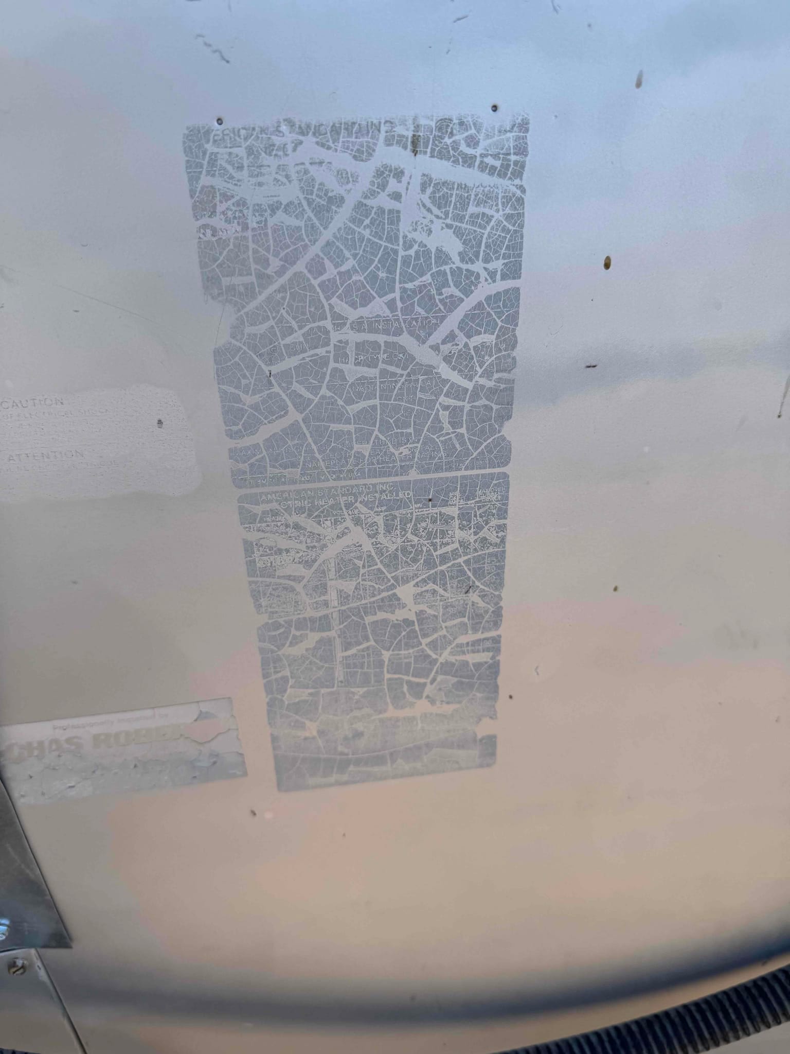 Weathered equipment label on outdoor condenser cabinet, text and model information faded and cracked across the sticker.
