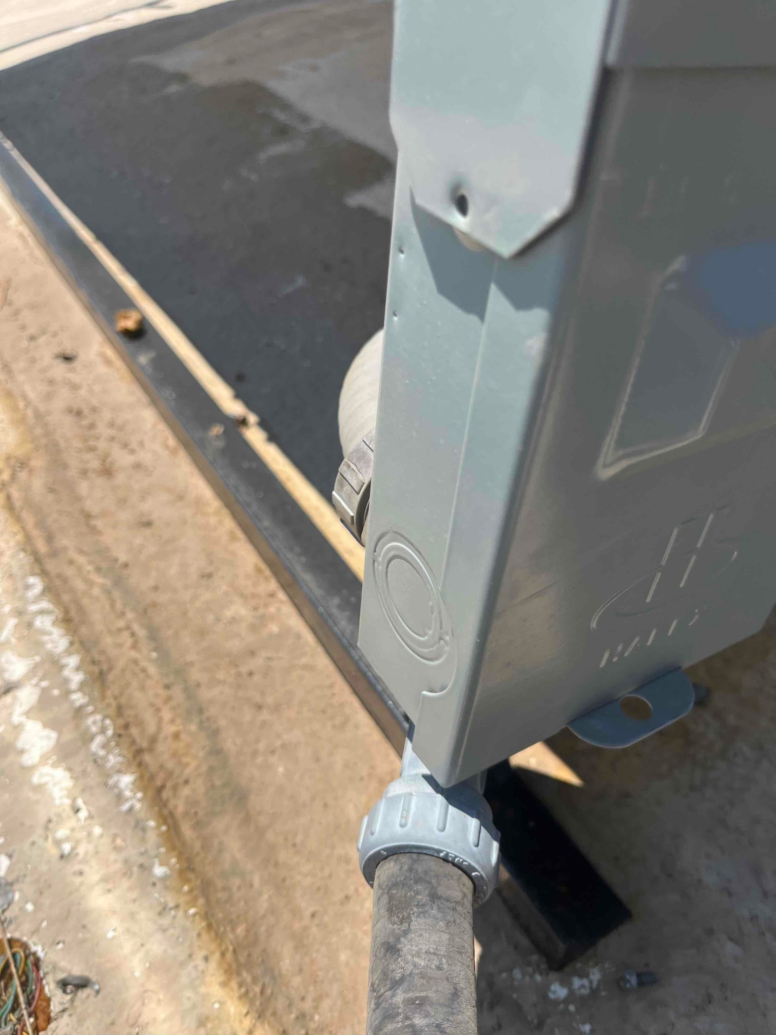 Weatherproof electrical box with flexible conduit entering through a watertight connector beside an outdoor equipment support rail.