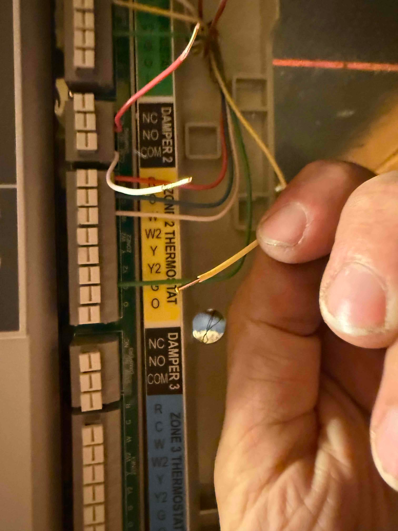 Zone control board terminals labeled for dampers and thermostats, with stripped red, white, and yellow wires being held for connection.