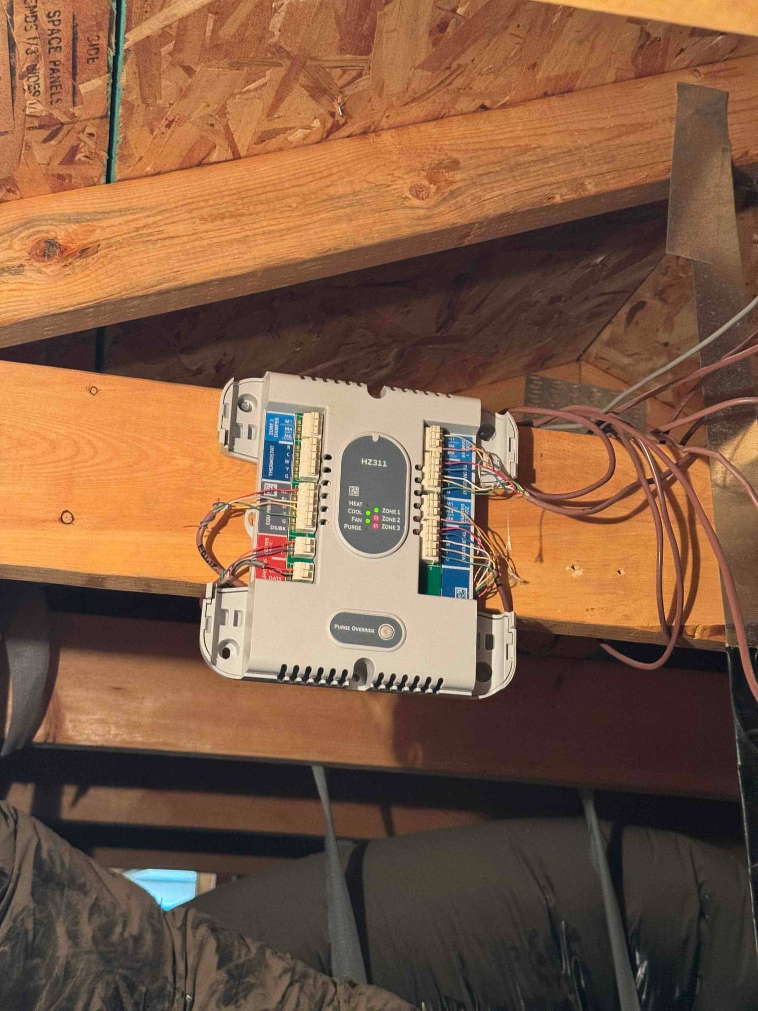 Zoning control panel mounted to a ceiling joist with multiple thermostat and damper wires connected, status indicator LEDs illuminated.