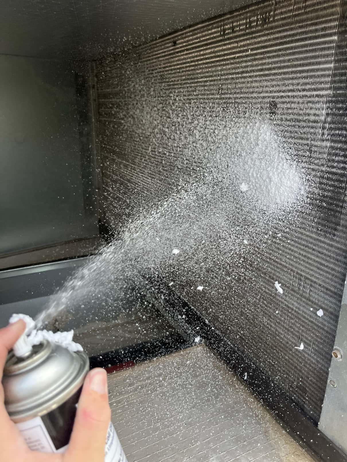 Aerosol spray is applied to the evaporator coil fins inside the air handler cabinet.