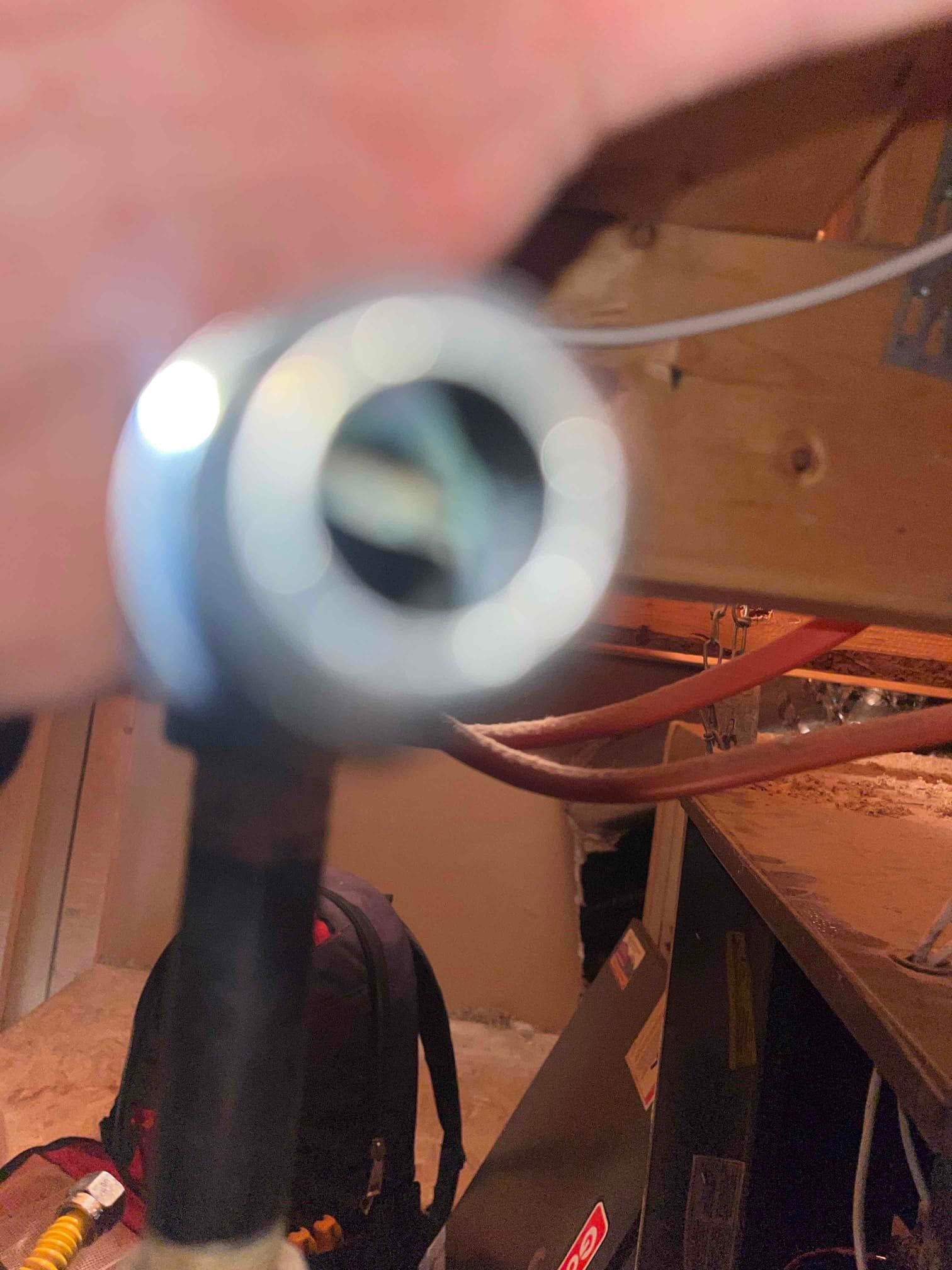 Air handler in attic with refrigerant lines and service tools visible; out-of-focus fitting in the foreground.