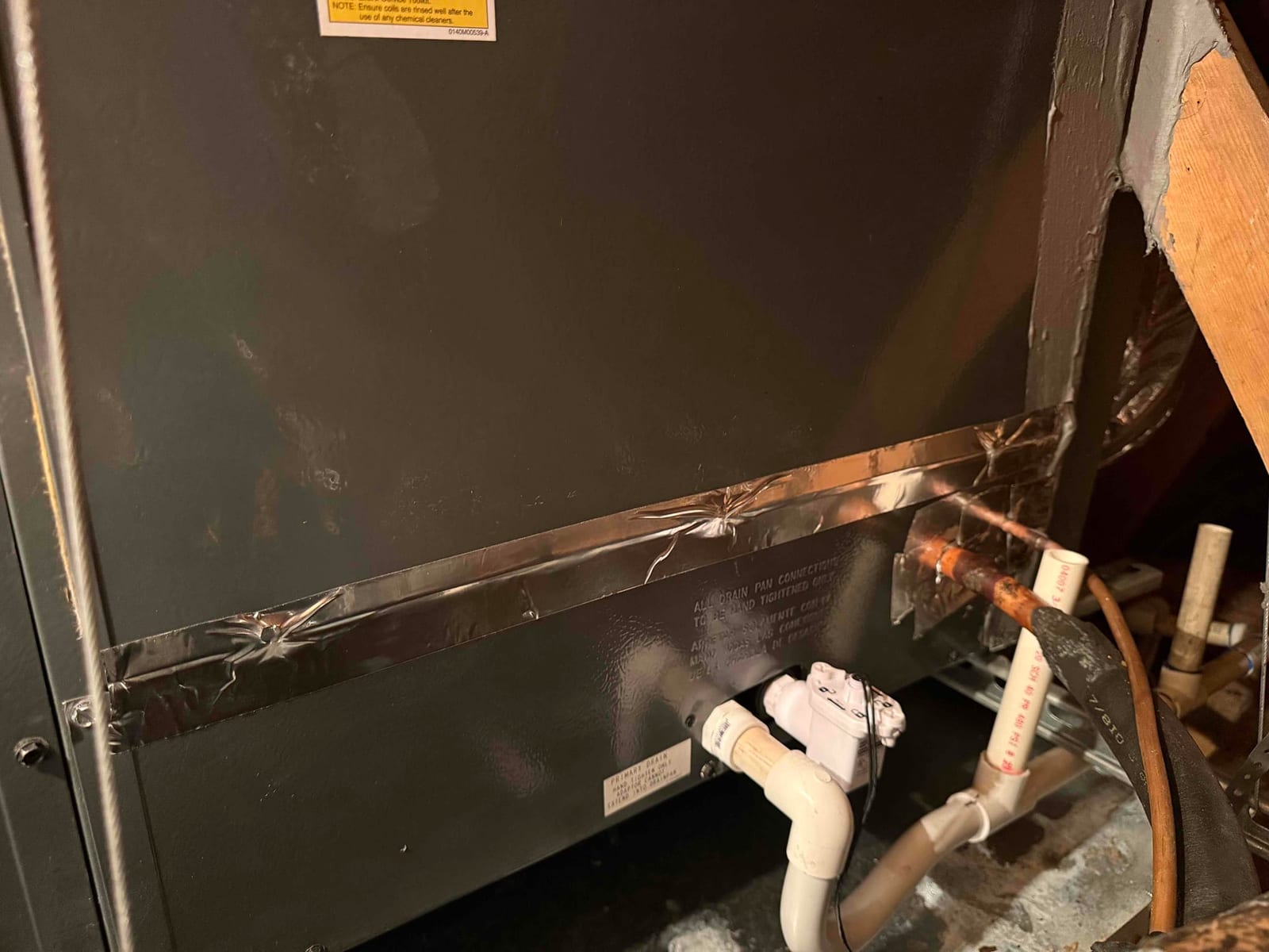 Air handler cabinet with foil tape on seam, copper refrigerant lines, and PVC condensate drain featuring a wired float switch.