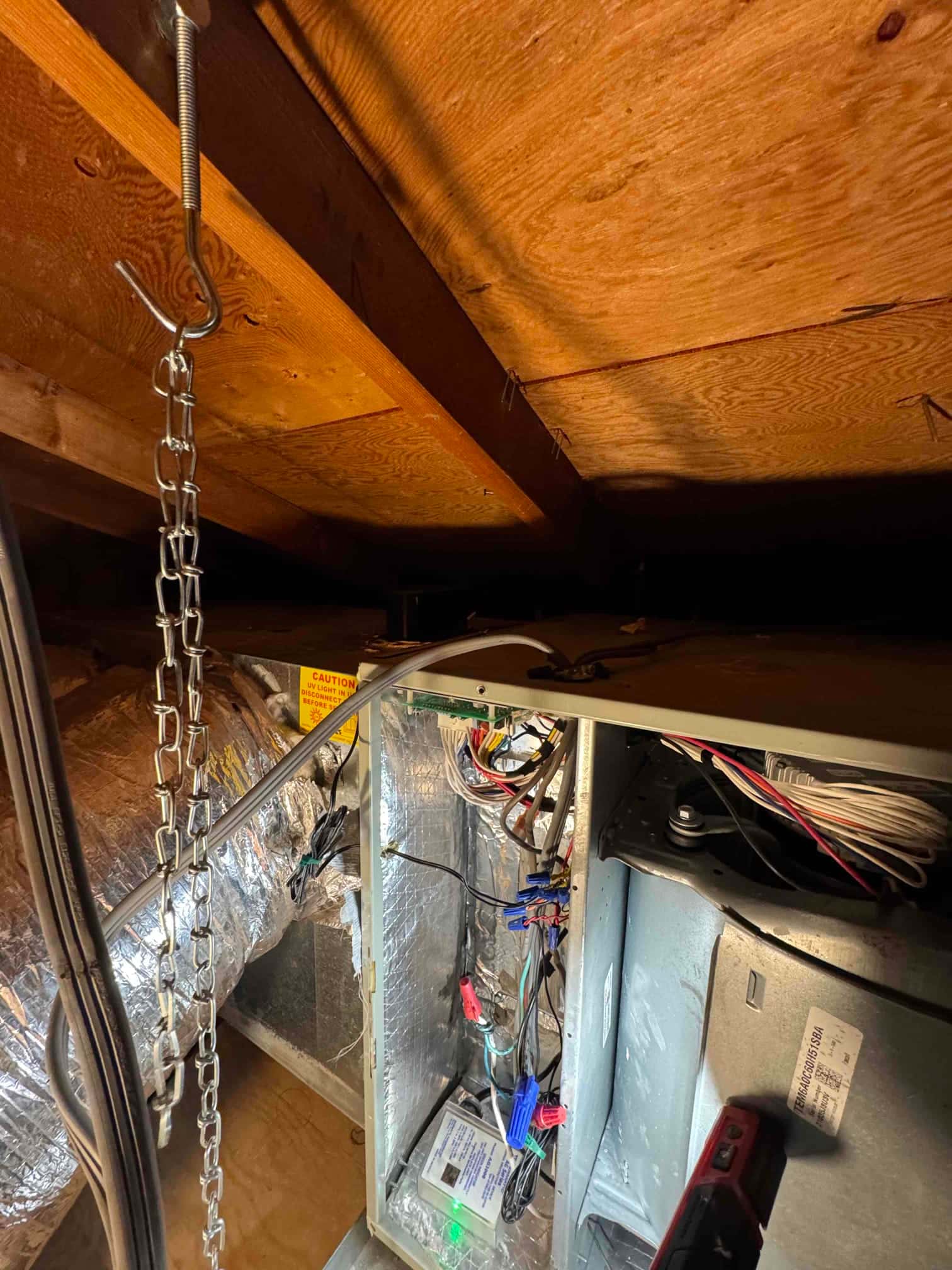 Air handler service panel open in attic, showing control wiring with multiple wire nuts and green indicator module.