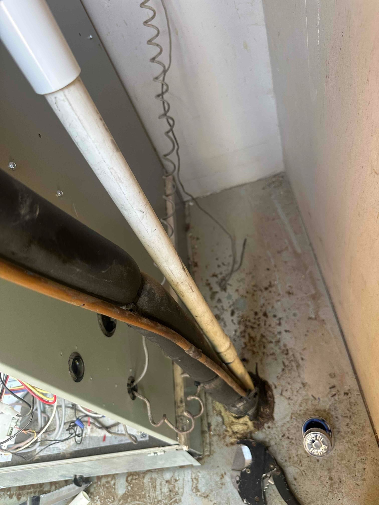 Air handler side with insulated refrigerant lines, copper liquid line, and PVC condensate drain at floor penetration.