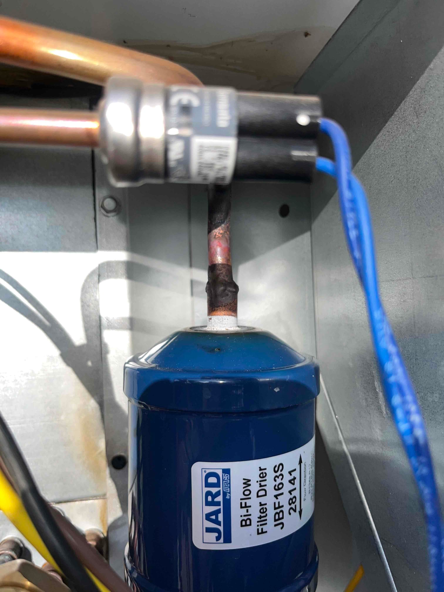 Bi-flow filter drier installed in the refrigerant line inside the unit, with copper tubing connections and nearby wires.