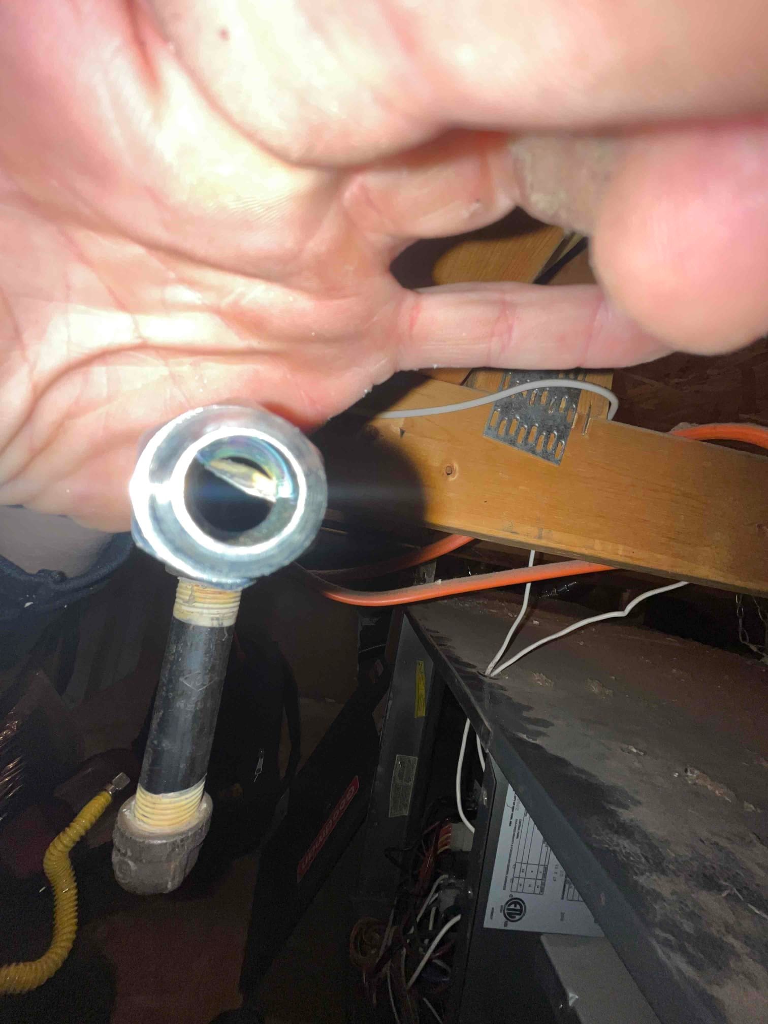Black iron gas pipe with threaded fittings in front of a furnace cabinet, with wiring and duct surfaces visible.