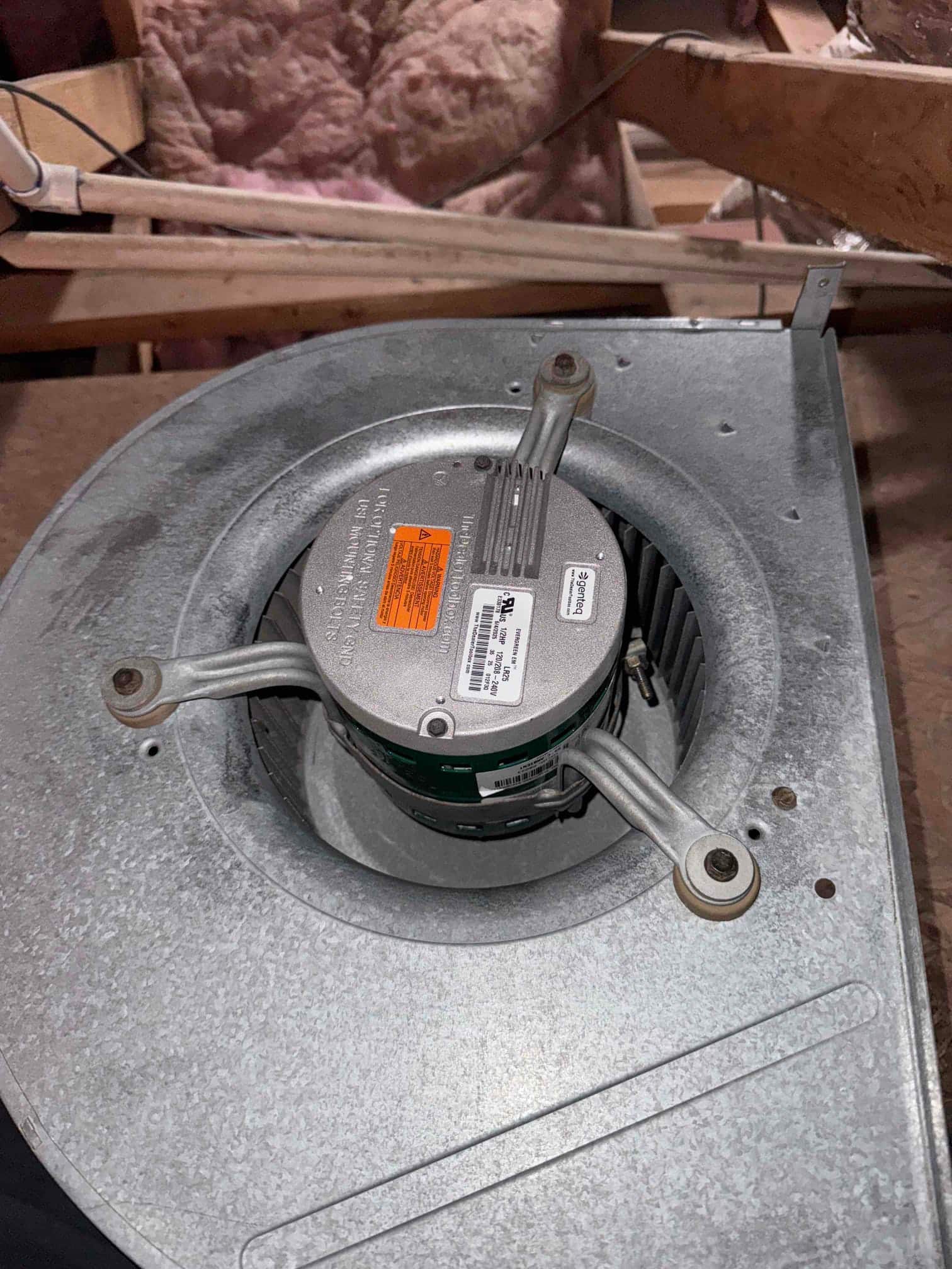 Blower wheel and motor assembly in galvanized housing, showing ECM motor with three mounting arms and attached labels.
