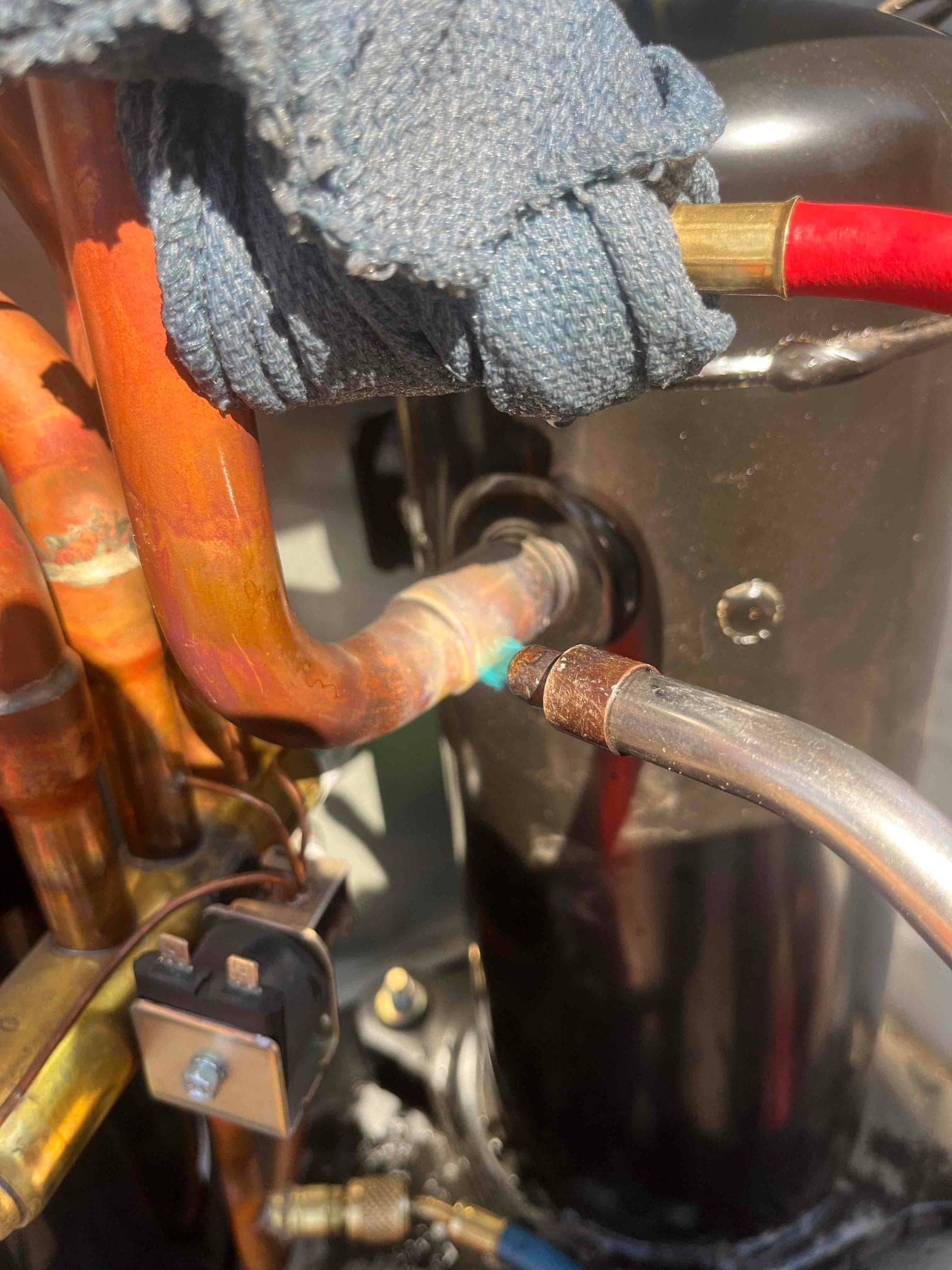 Close-up of compressor connections with copper refrigerant lines, brazed joints, and a small two-terminal switch mounted on the tubing.