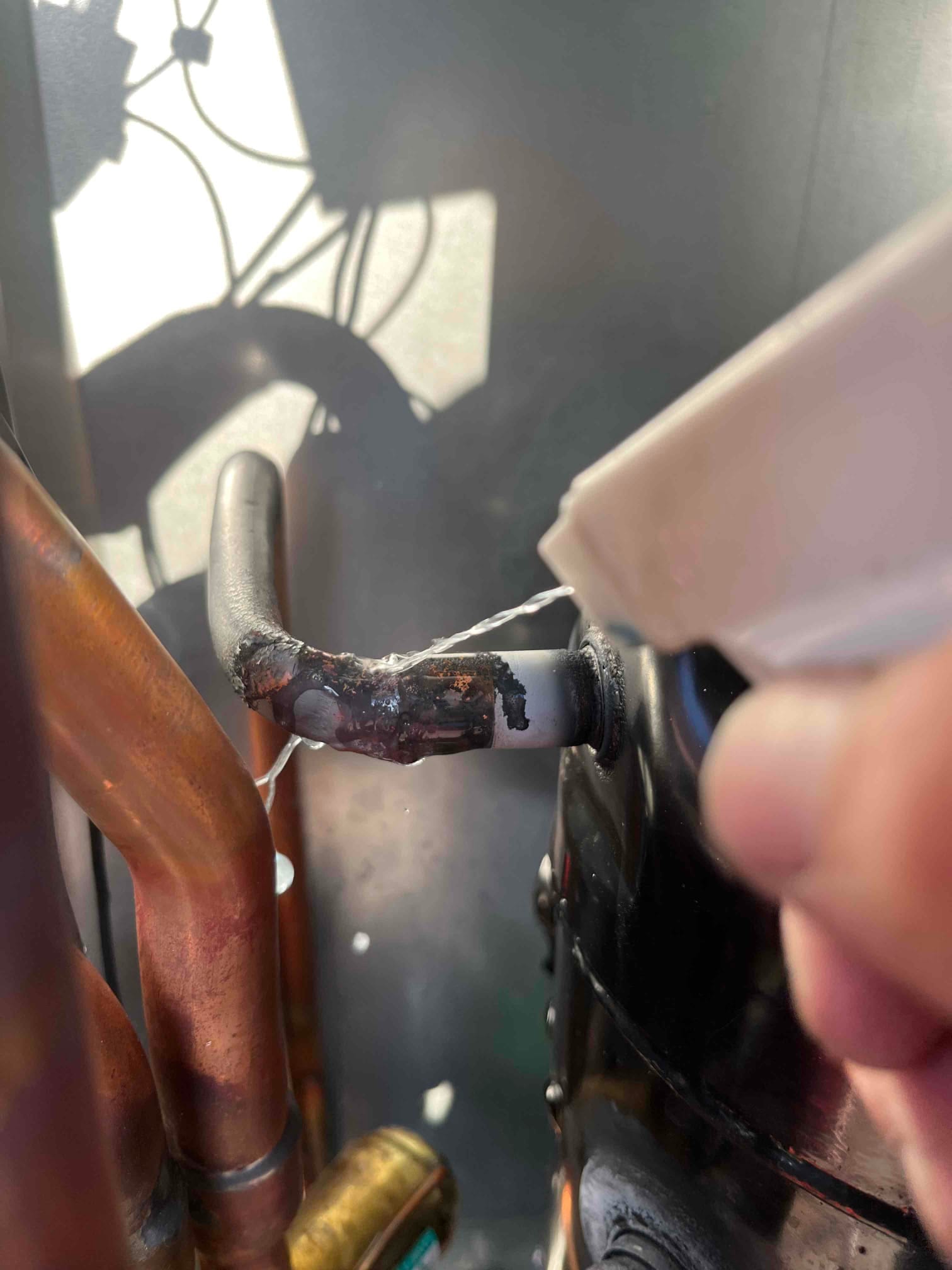 Close-up of compressor tubing connection with darkened brazed joint while soap solution is applied.