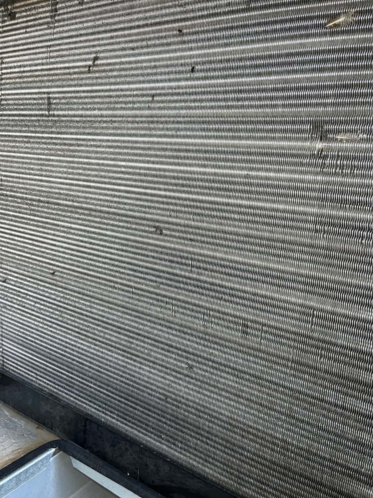 Close-up of evaporator coil fins above the drain pan inside the air handler cabinet.