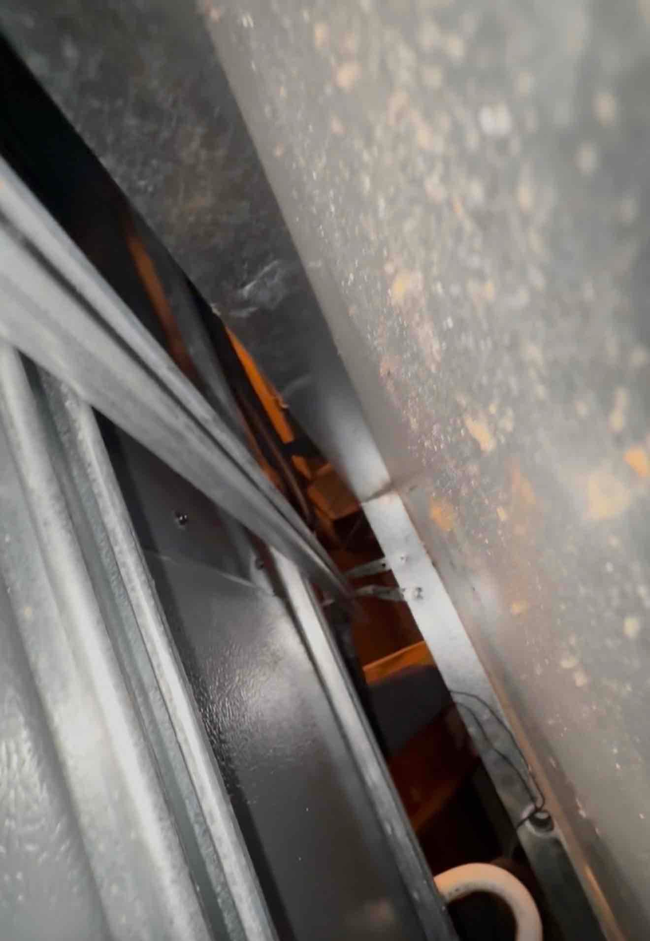 Close-up inside a metal HVAC cabinet showing sheet metal surfaces, wiring, and rust spots along an edge.