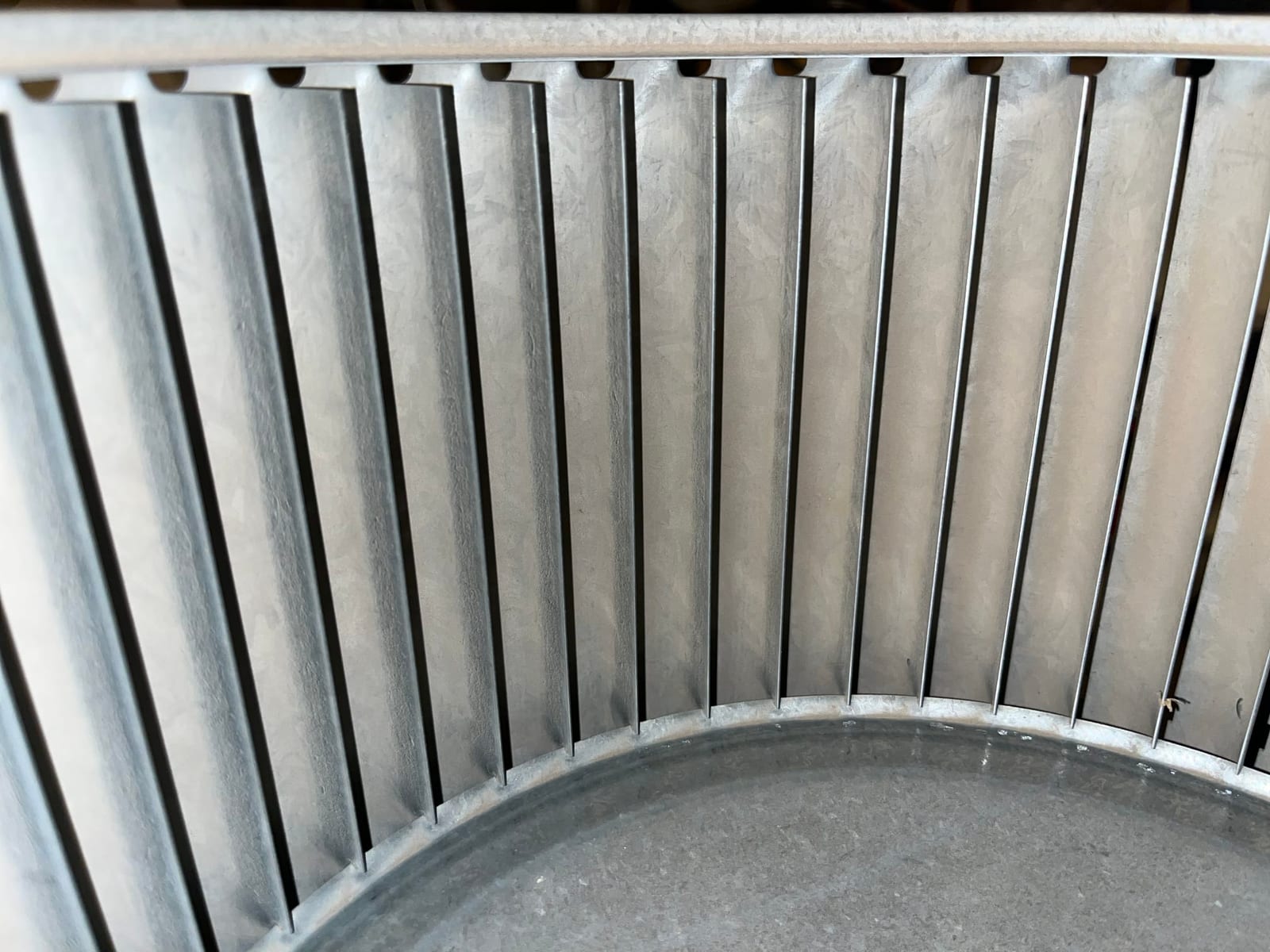 Close-up of a metal blower wheel with evenly spaced blades and circular rim inside the housing.