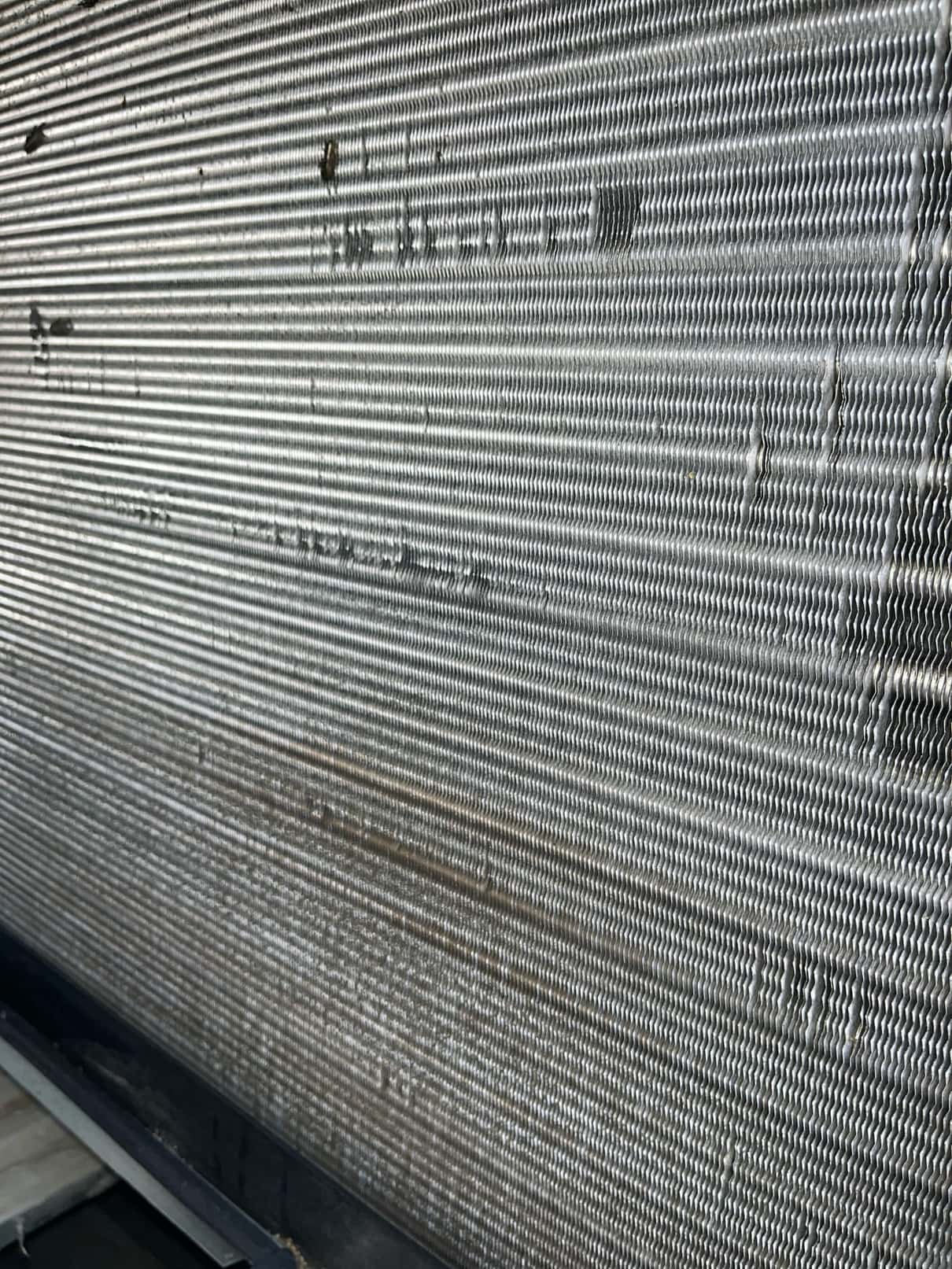 Close-up of an outdoor condenser coil with aluminum fins, showing areas of bent fins and dirt streaks.
