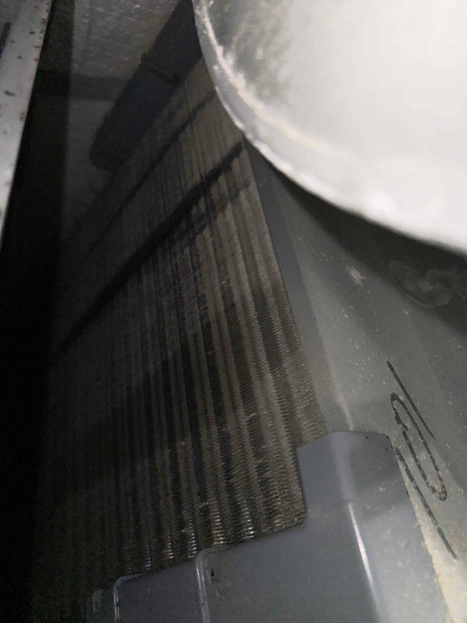 Close-up view of evaporator coil fins inside an air handler, with dust visible on surrounding metal and plastic surfaces.