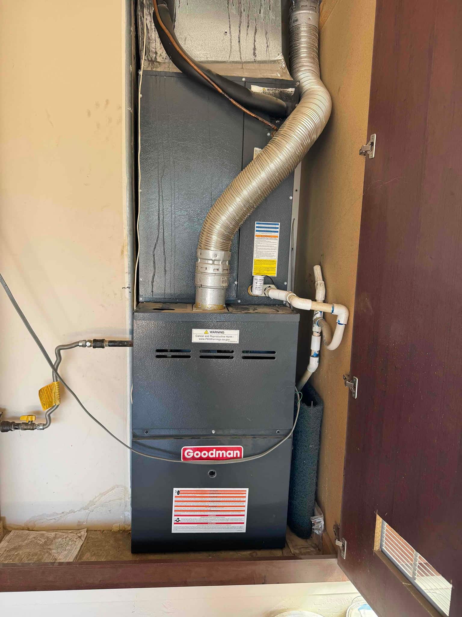 Closet-mounted furnace and evaporator cabinet with flexible vent, gas line, insulated refrigerant line, and PVC condensate drain piping visible.