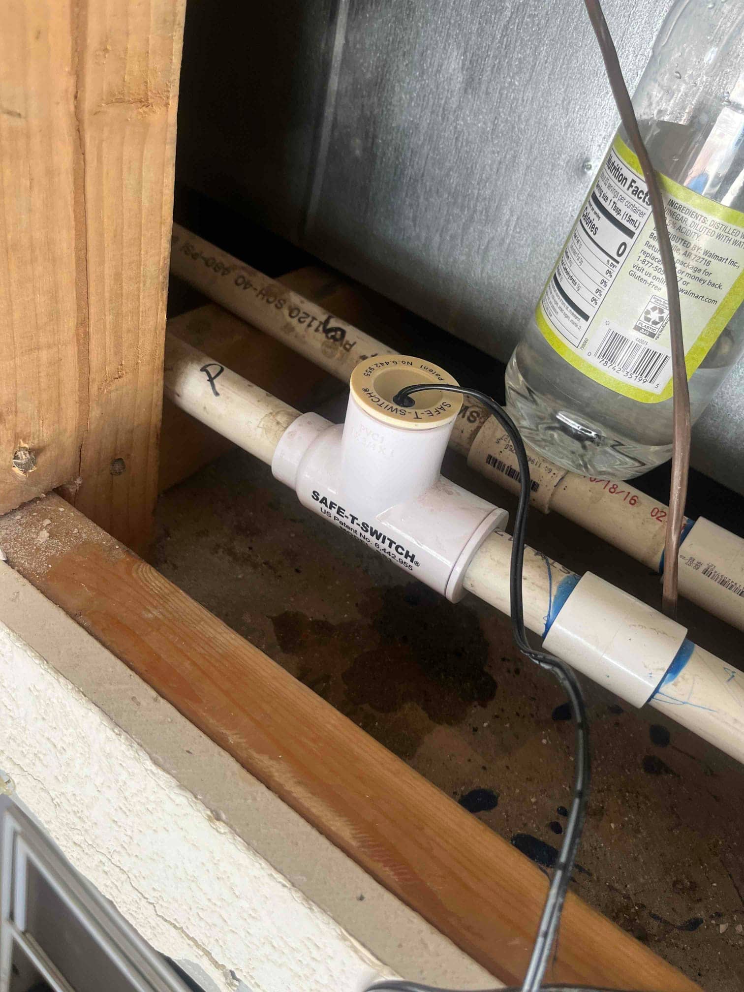 Condensate drain line with inline float safety switch installed, wiring connected, blue PVC primer at joints, wet pan beneath.