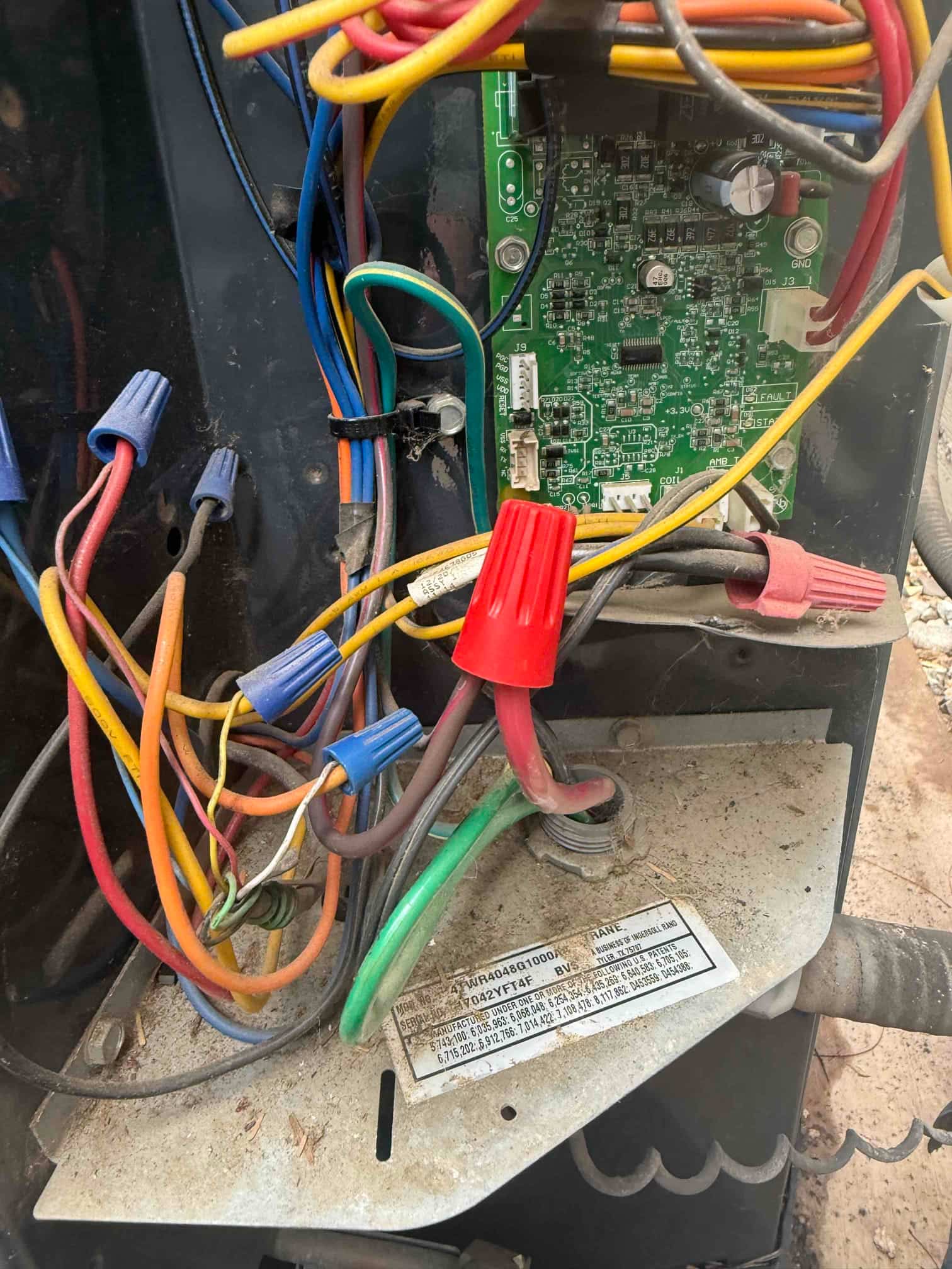 Condenser electrical compartment showing control board, multiple colored conductors with wire nuts, and a green ground wire on the chassis.