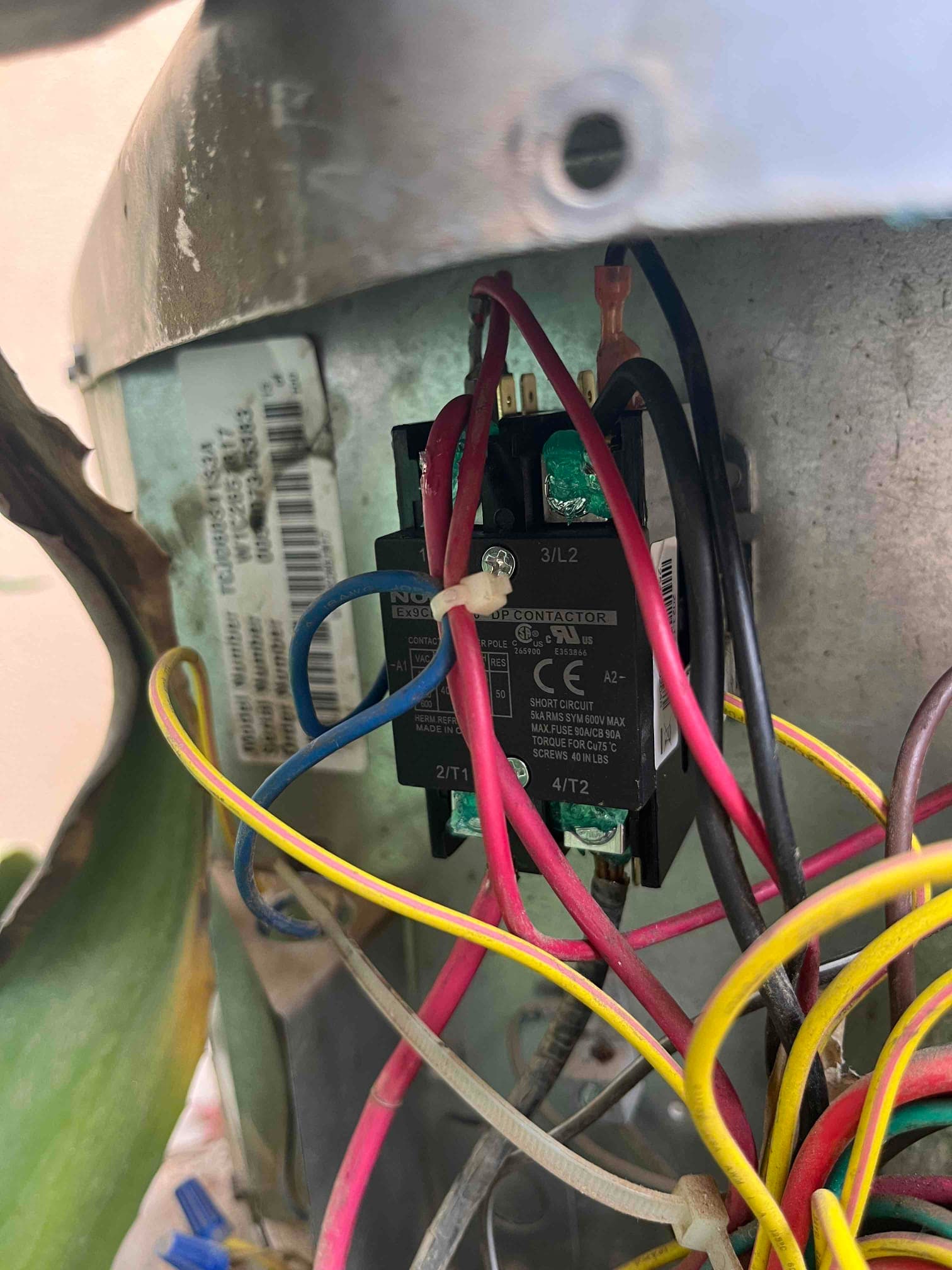 Contactor with multiple connected wires inside the outdoor condenser electrical compartment, showing green corrosion on lower terminals.