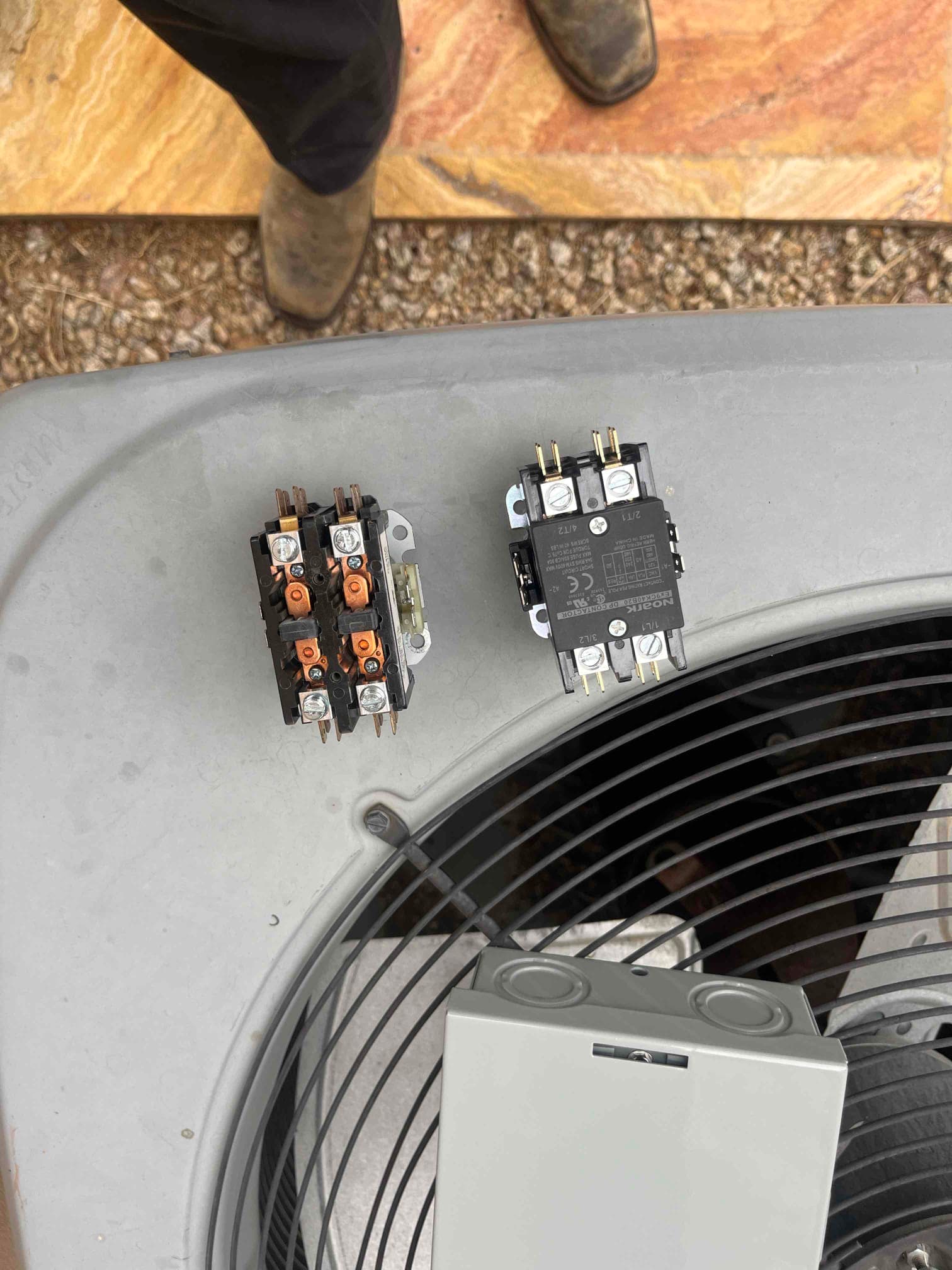 Two contactors sit on the outdoor condenser top, with one showing dark discoloration and wear at the terminals.