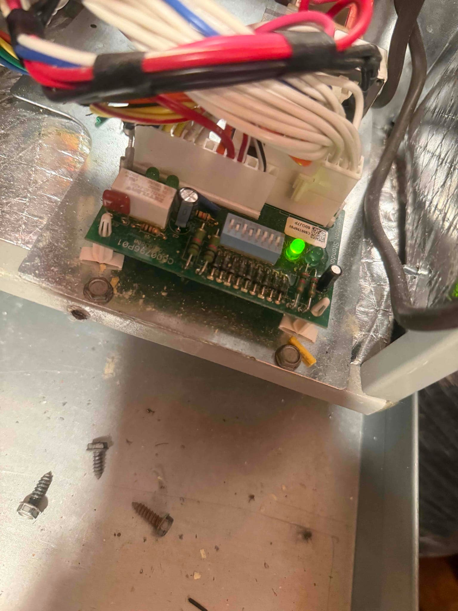 Control board inside air handler with connected wiring harness, DIP switch block, and green status LED illuminated. Loose screws nearby.