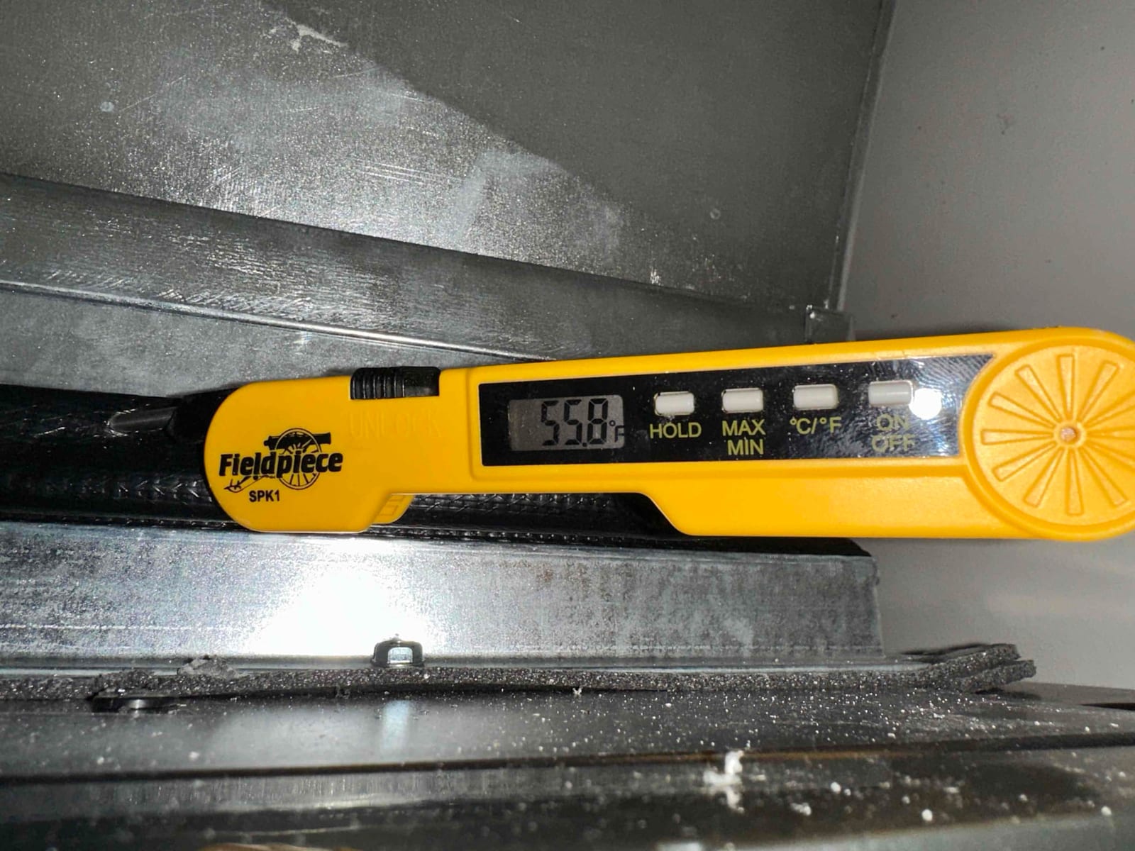 Digital thermometer probe measures 55.8 degrees Fahrenheit at the supply outlet inside the duct during cooling operation.