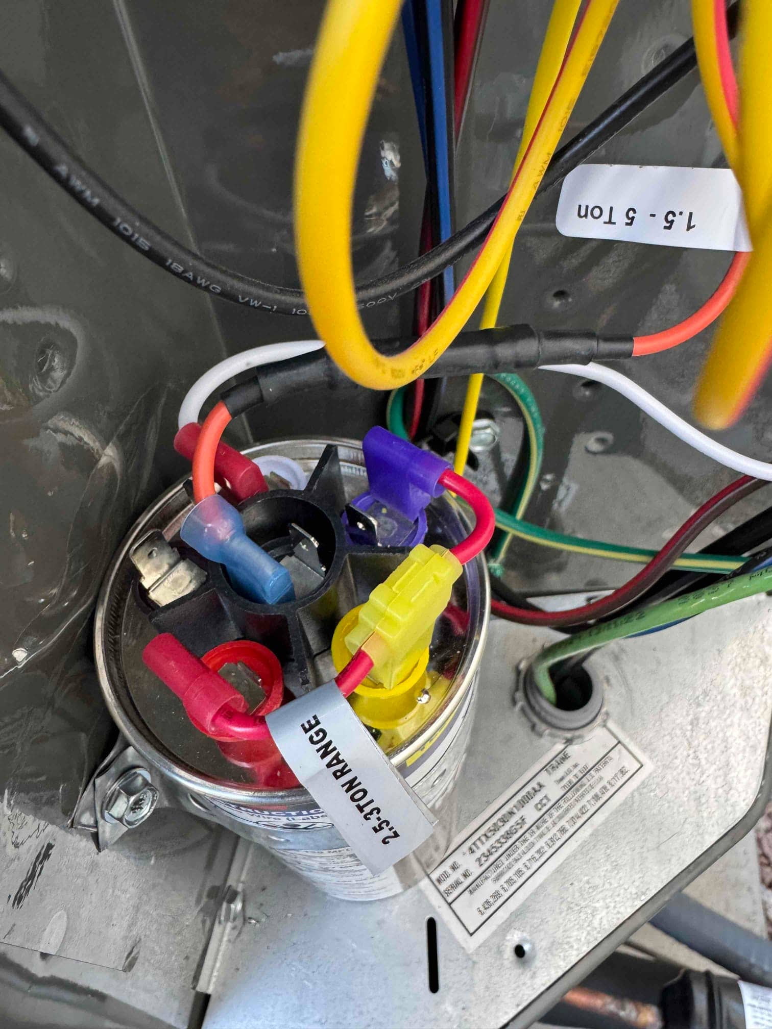 Dual-run capacitor with color-coded terminals and connected wiring inside the outdoor condenser control compartment.