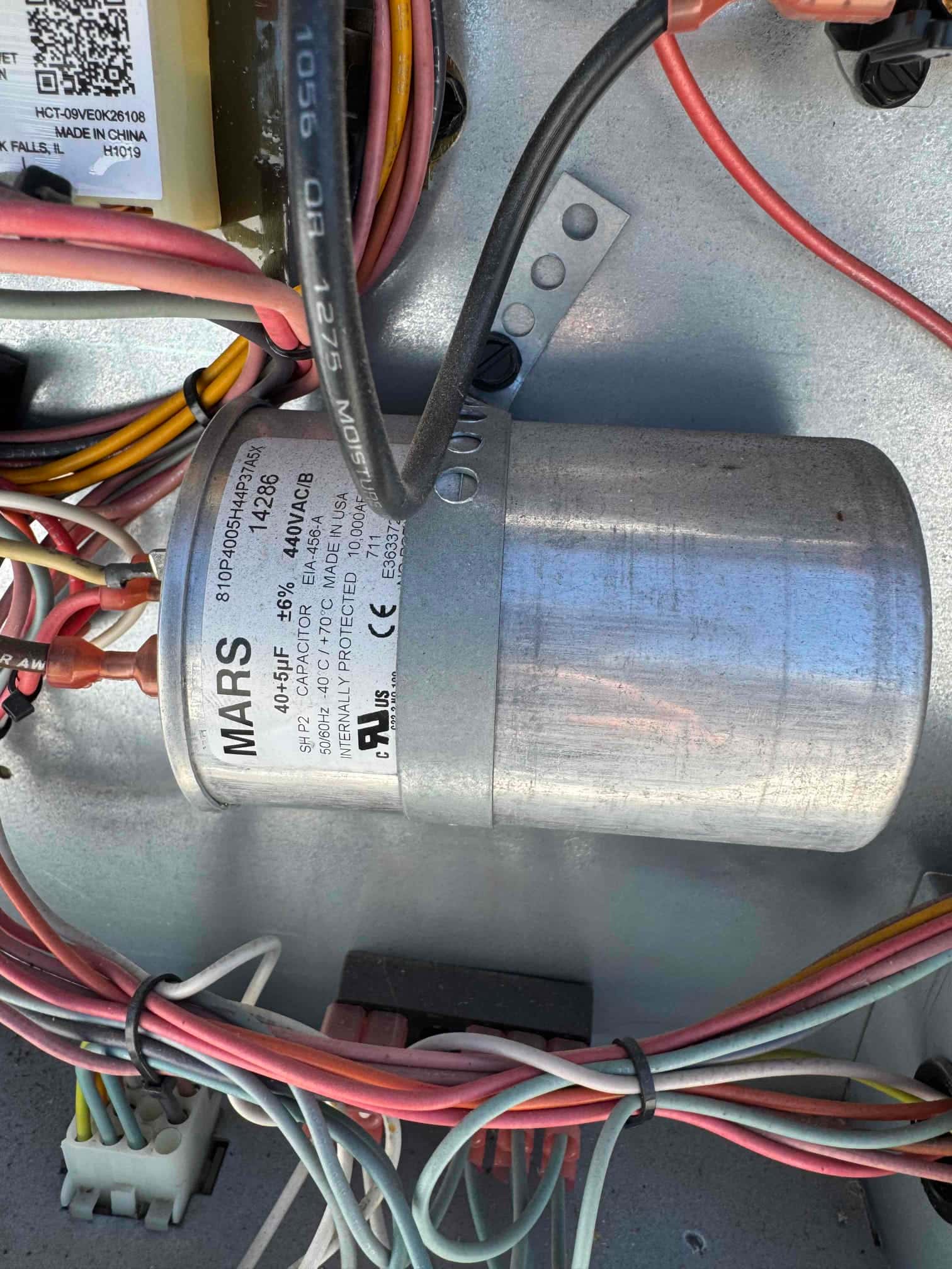 Dual-run capacitor labeled 40/5 μF 440VAC with wires connected to its terminals inside the condenser.