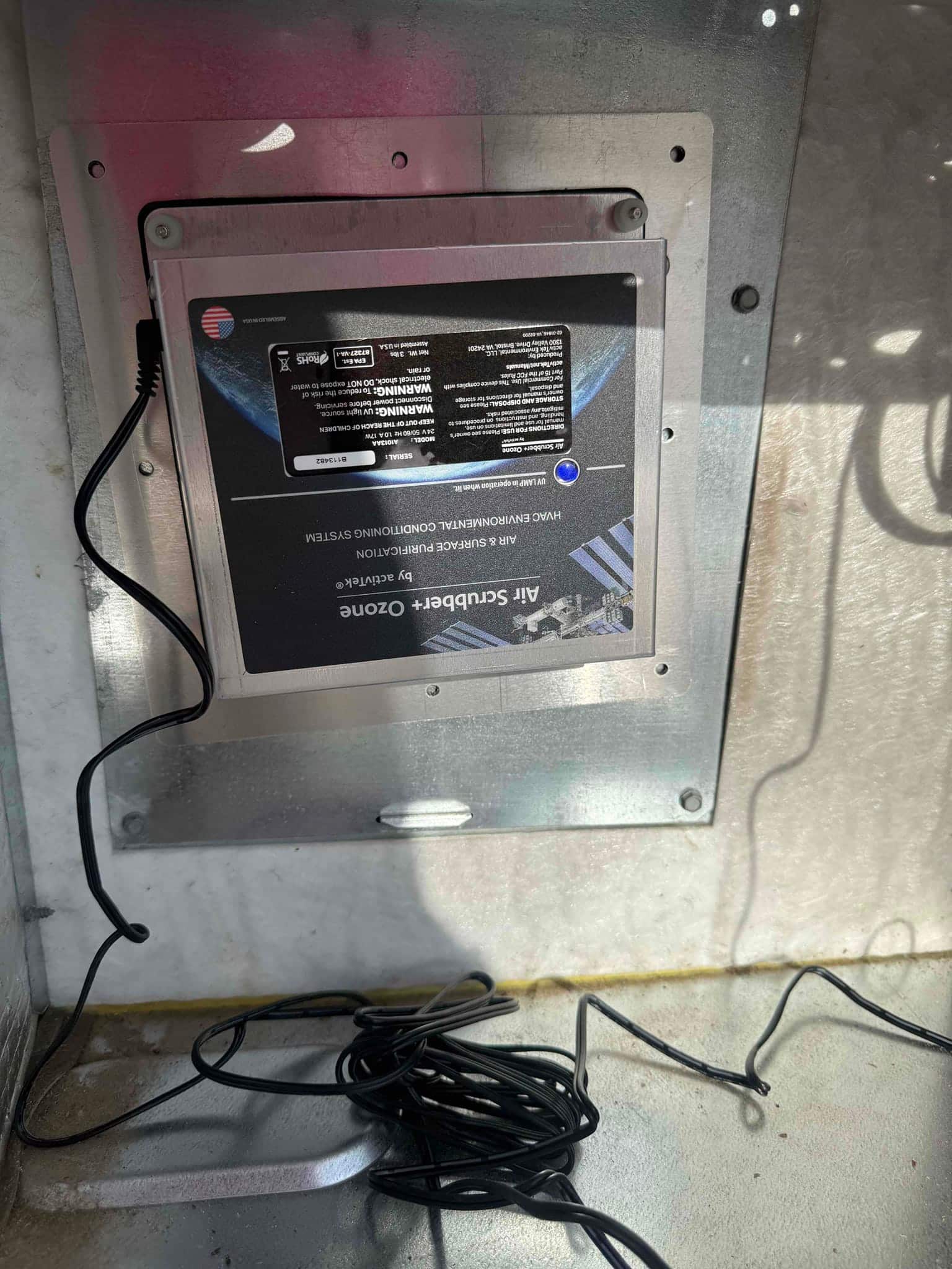 Duct-mounted air purification module installed on a galvanized panel, with black wiring coiled at the bottom.