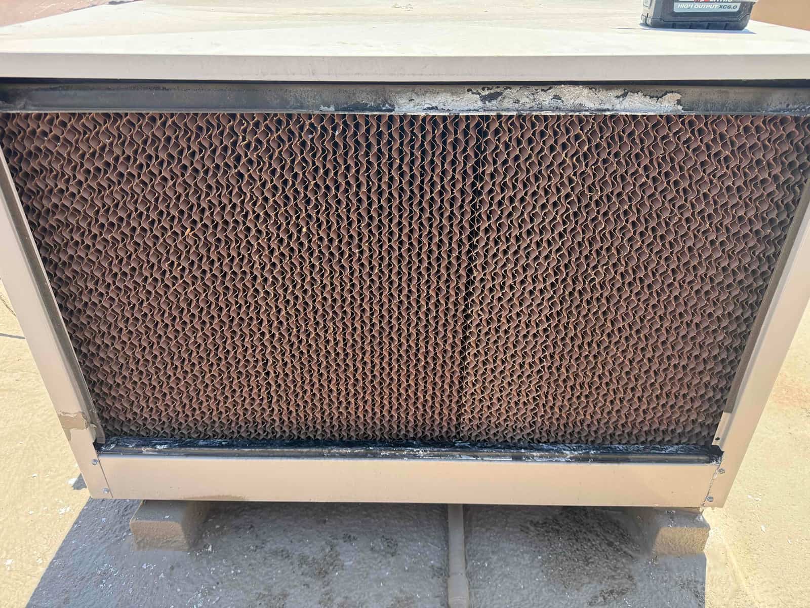 Evaporative cooler media panel in rooftop housing, showing uniform pad surface and white mineral buildup along the top.