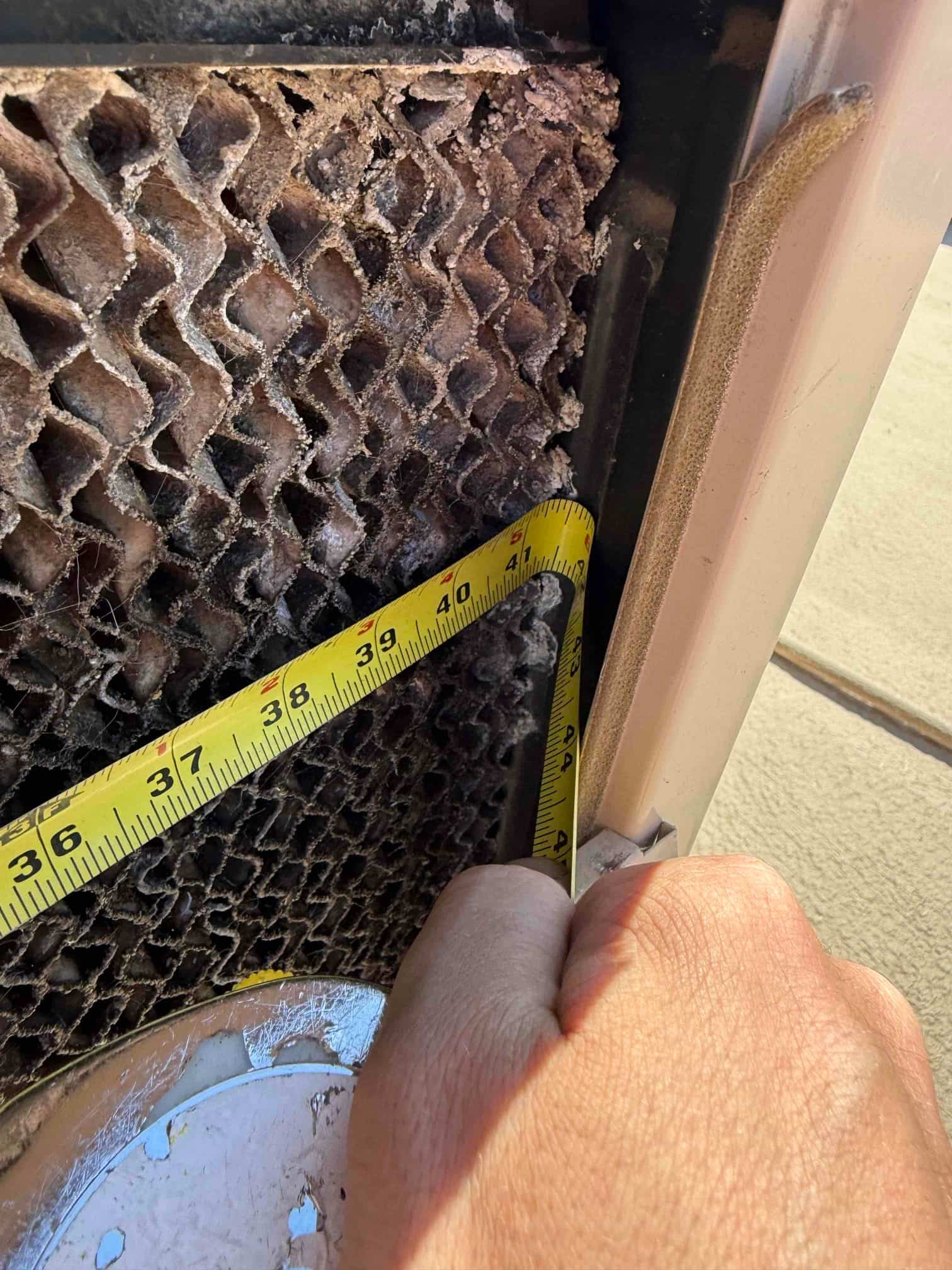 Evaporative cooler pad with heavy mineral buildup as a tape measure checks the pad thickness.
