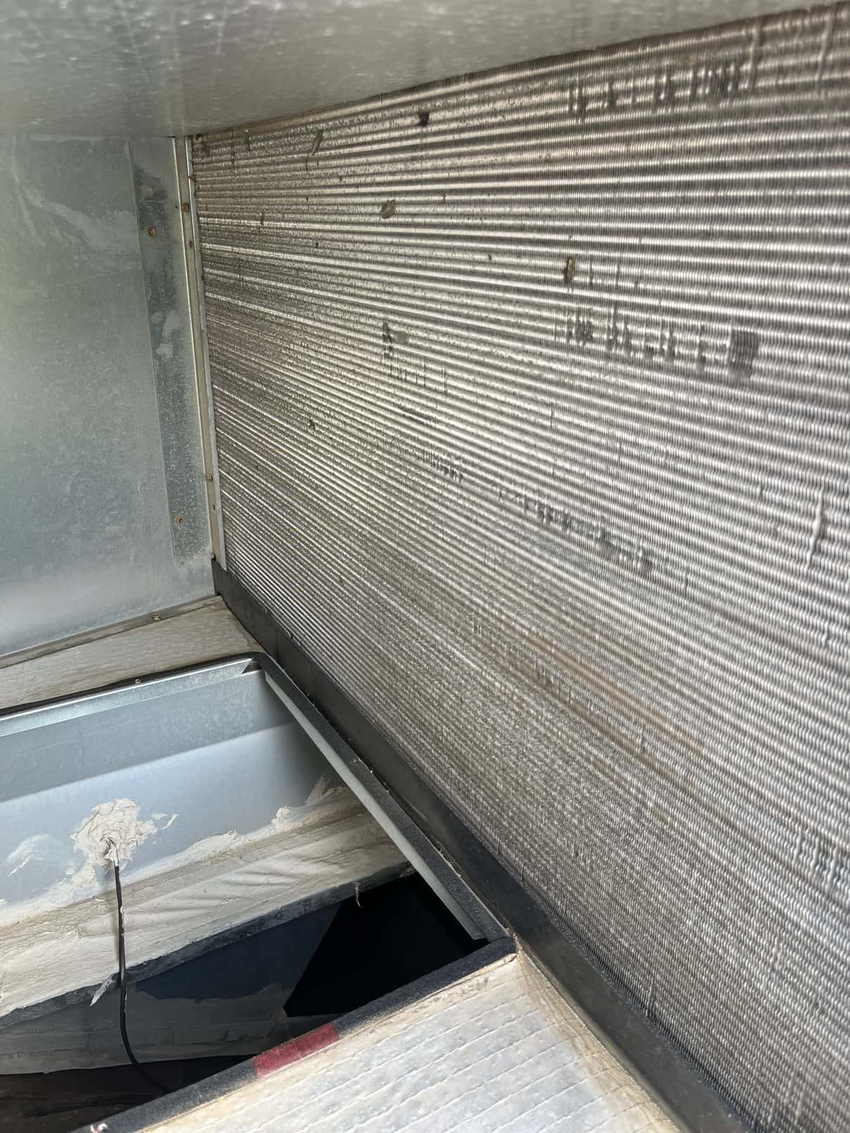 Evaporator coil surface with aluminum fins inside the air handler cabinet, with scattered bent fins and light debris.